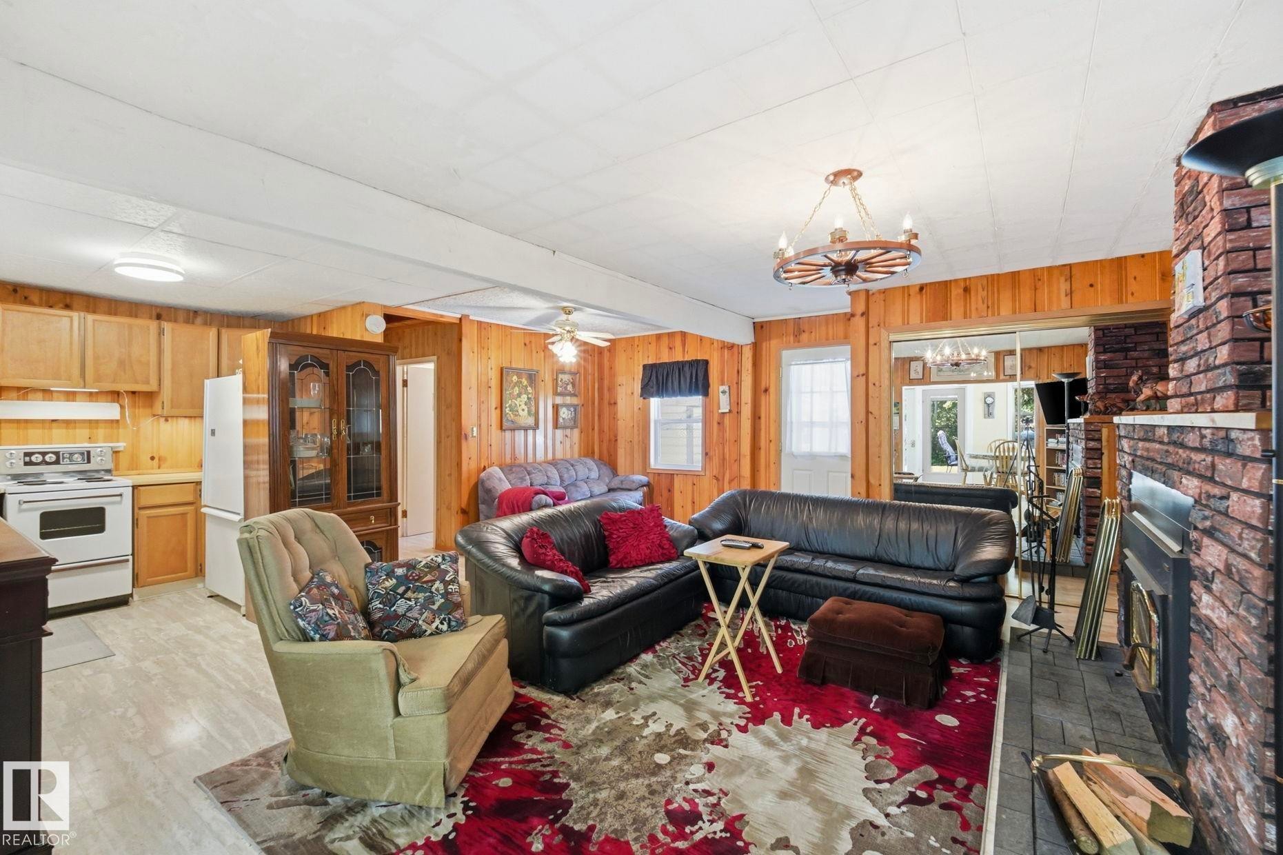 Open concept living area featuring wood-finish wall paneling, a brick fireplace, and wood-finish flooring - 1410 47436 Range Rd. 15, Rural Leduc County, AB