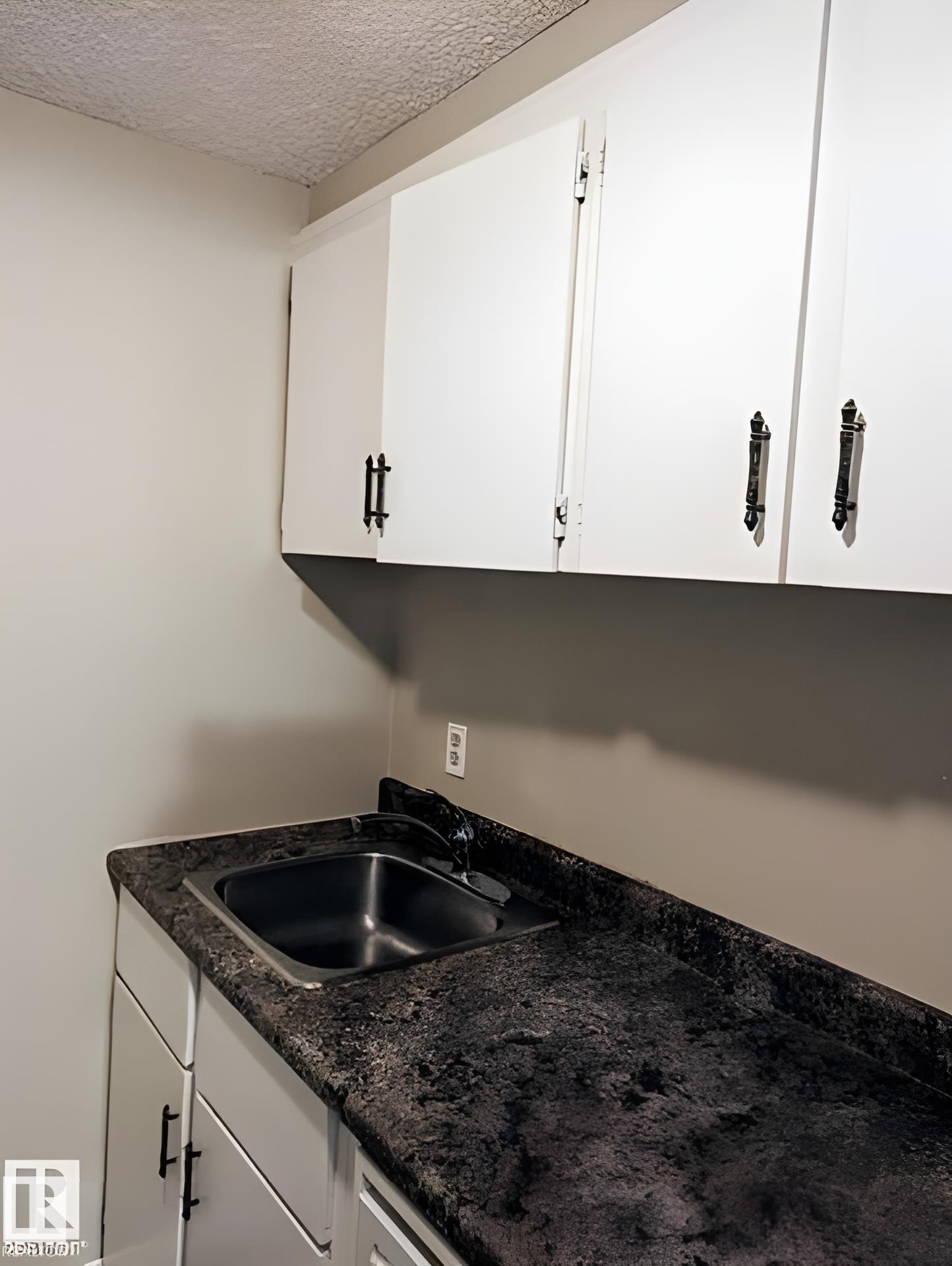 Utility area featuring a stainless steel sink, dark speckled countertop, and white cabinetry with black hardware - 611 12831 66 Street, Edmonton, AB