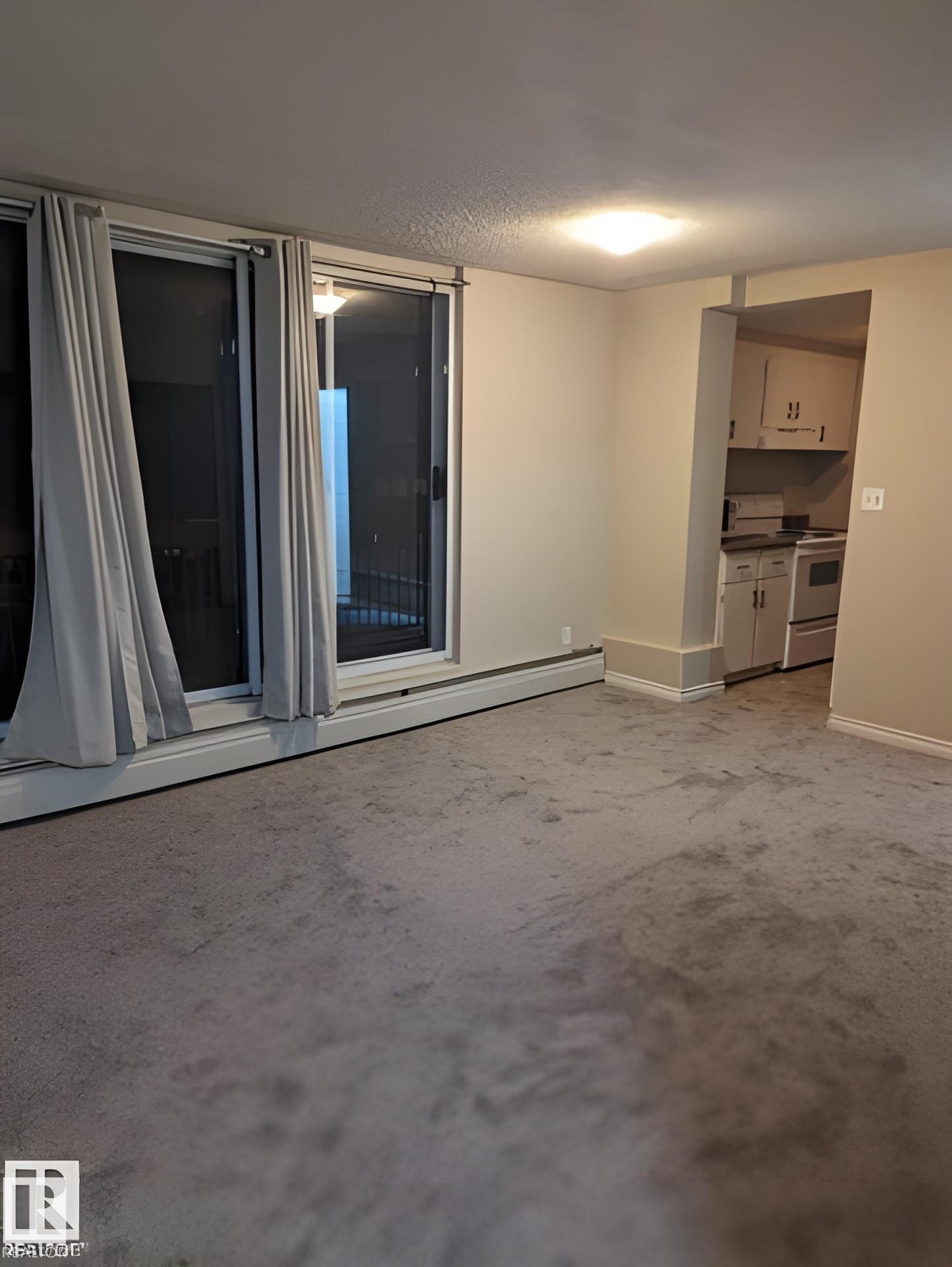 Sliding glass doors with window treatments, recessed kitchen area with white cabinetry, wall-to-wall carpeting, and neutral wall paint - 611 12831 66 Street, Edmonton, AB