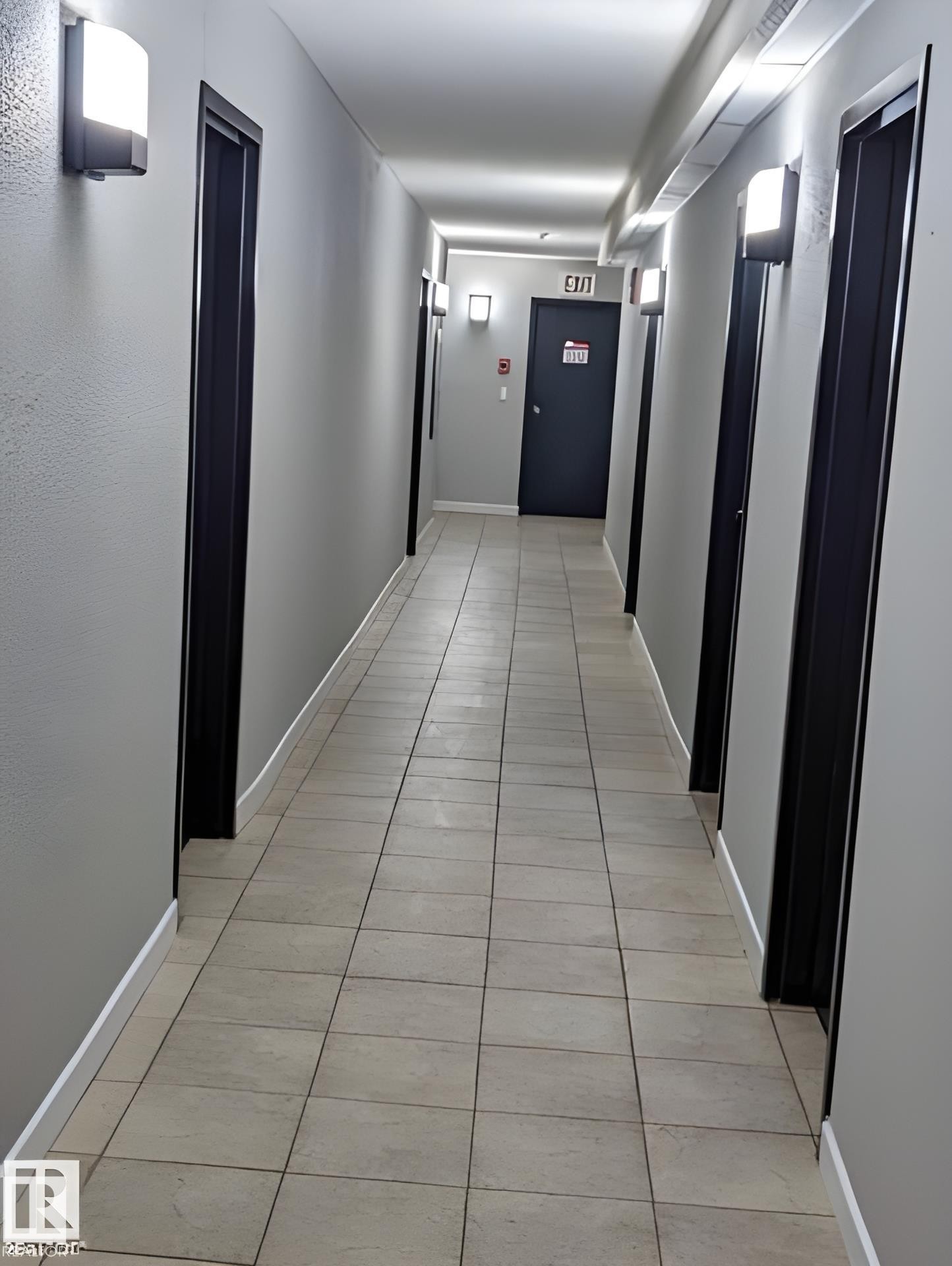 Hallway with light gray walls, dark door frames, and sconce lighting - 611 12831 66 Street, Edmonton, AB