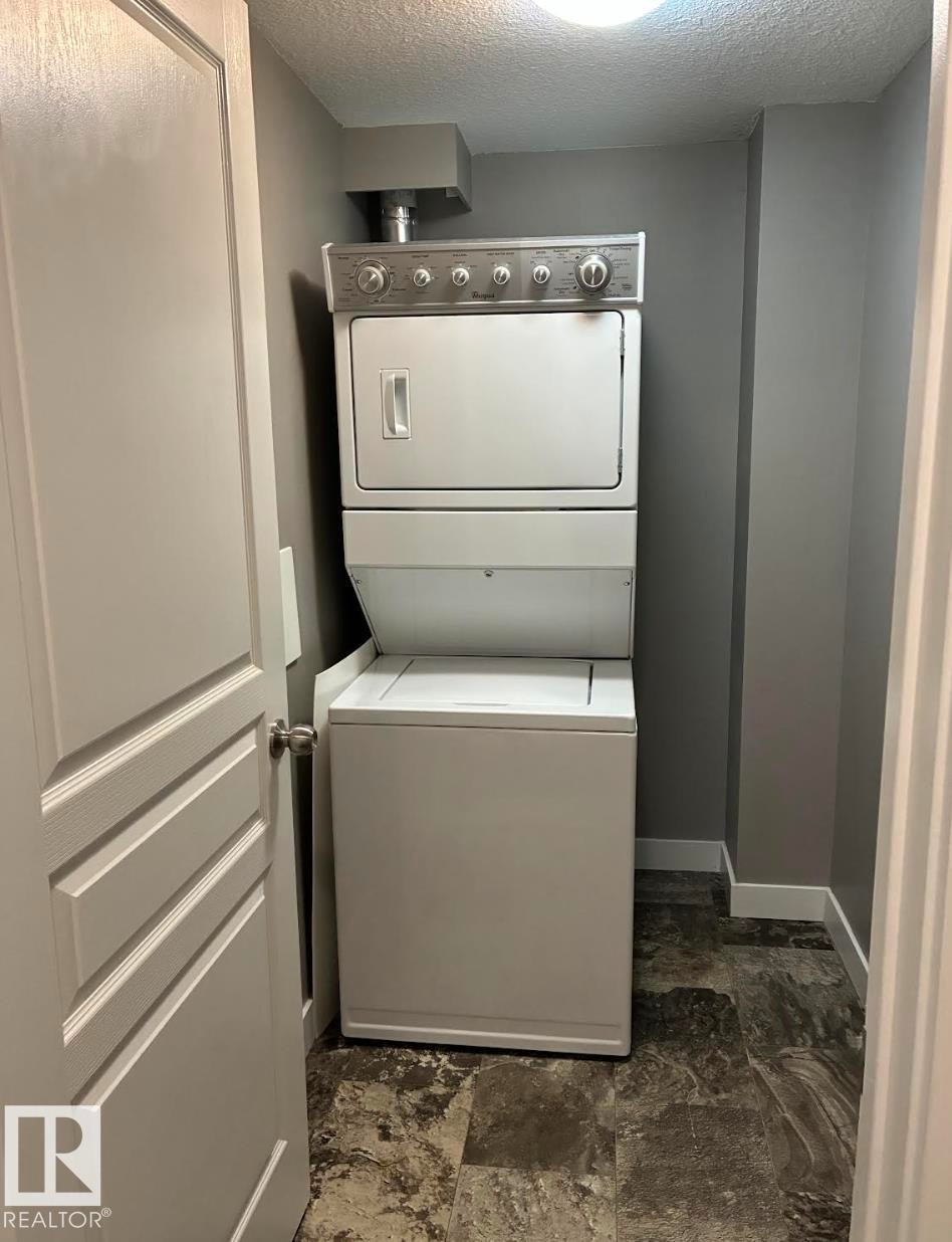 Dedicated laundry area featuring a stacked washer and dryer unit, gray wall paint, white baseboards, and patterned flooring - #210 3670 139 Av Nw, Edmonton, AB - Indoor Photo Showing Laundry Room