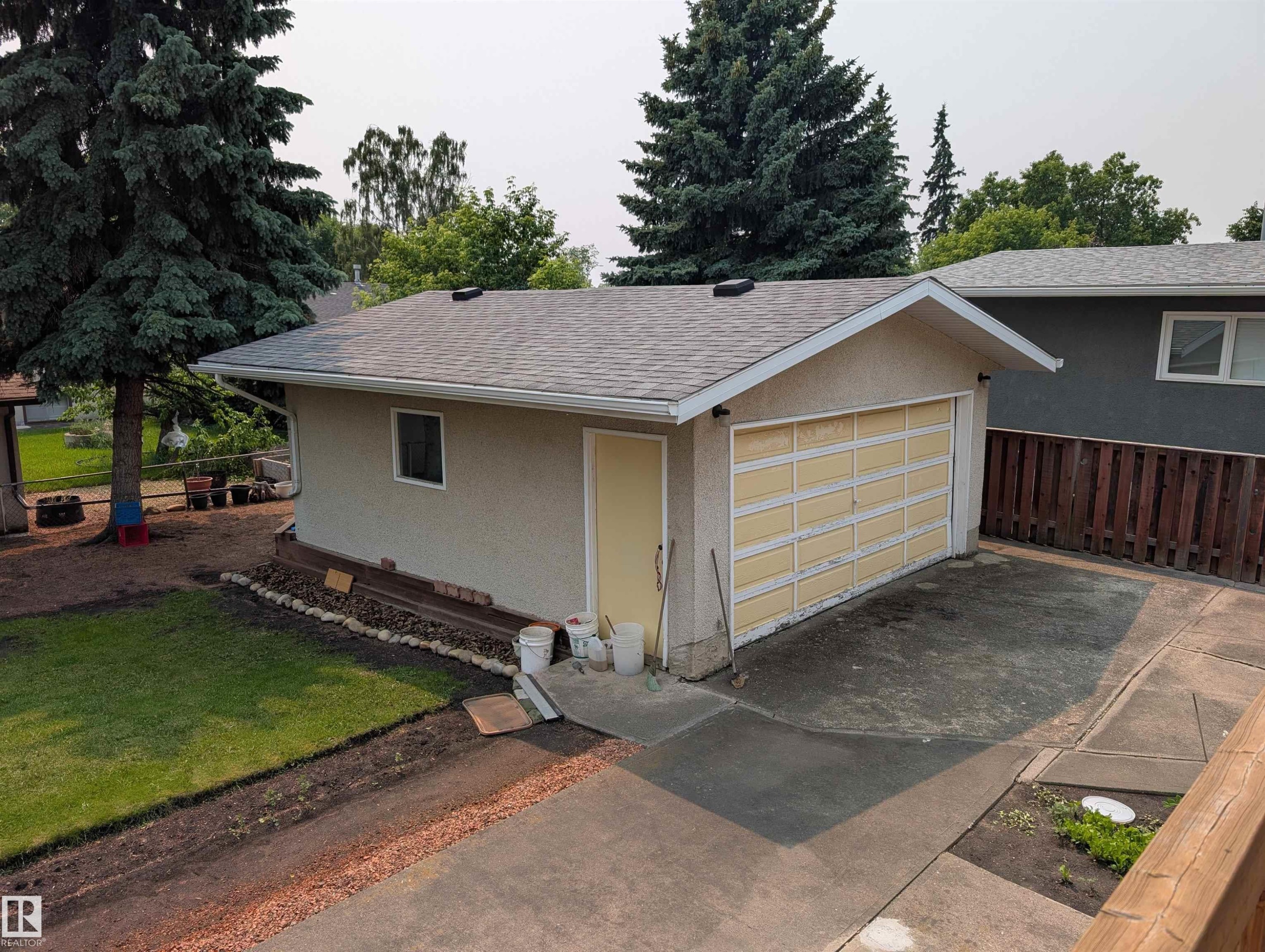 Detached garage featuring a paneled overhead door, stucco exterior, shingled roof, and an adjacent concrete driveway - 6415 147 Avenue, Edmonton, AB