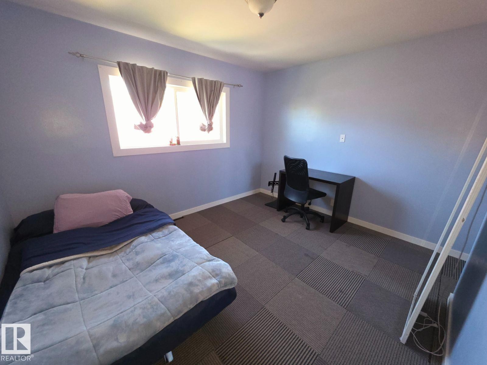 Bedroom featuring a window with white trim, light blue walls, and patterned carpet tile flooring - 10404 116 Avenue, Edmonton, AB