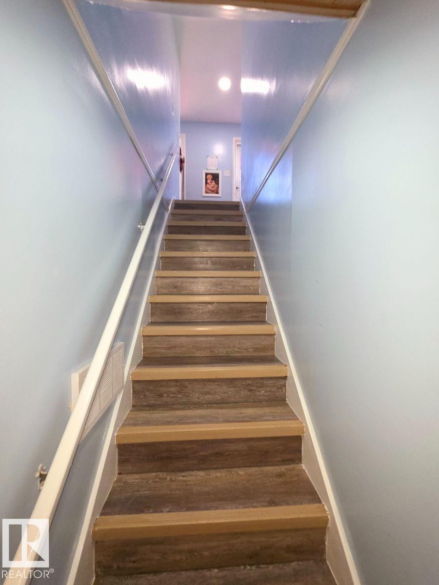 Staircase with wood-finish treads and risers, light blue wall paint, and white handrails - 10404 116 Avenue, Edmonton, AB