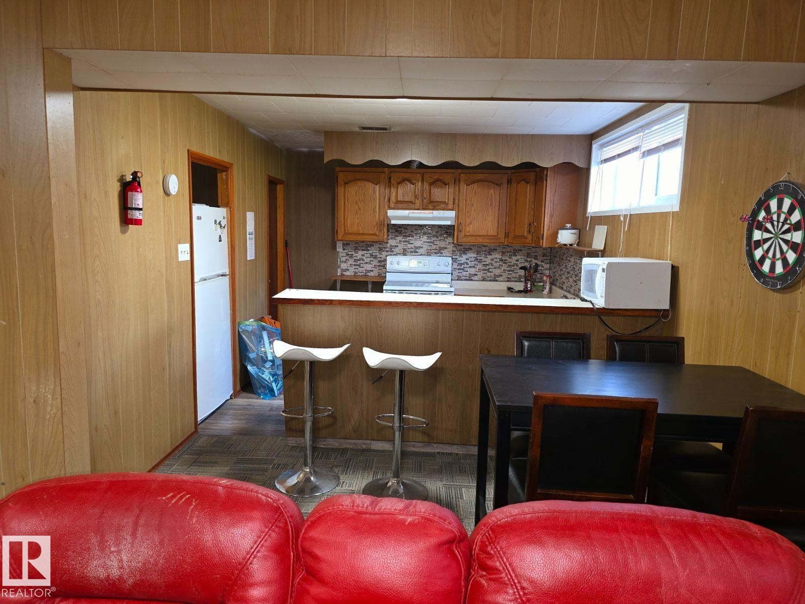 Kitchenette with wood-finish paneling, wood cabinetry, and a patterned tile backsplash - 10404 116 Avenue, Edmonton, AB