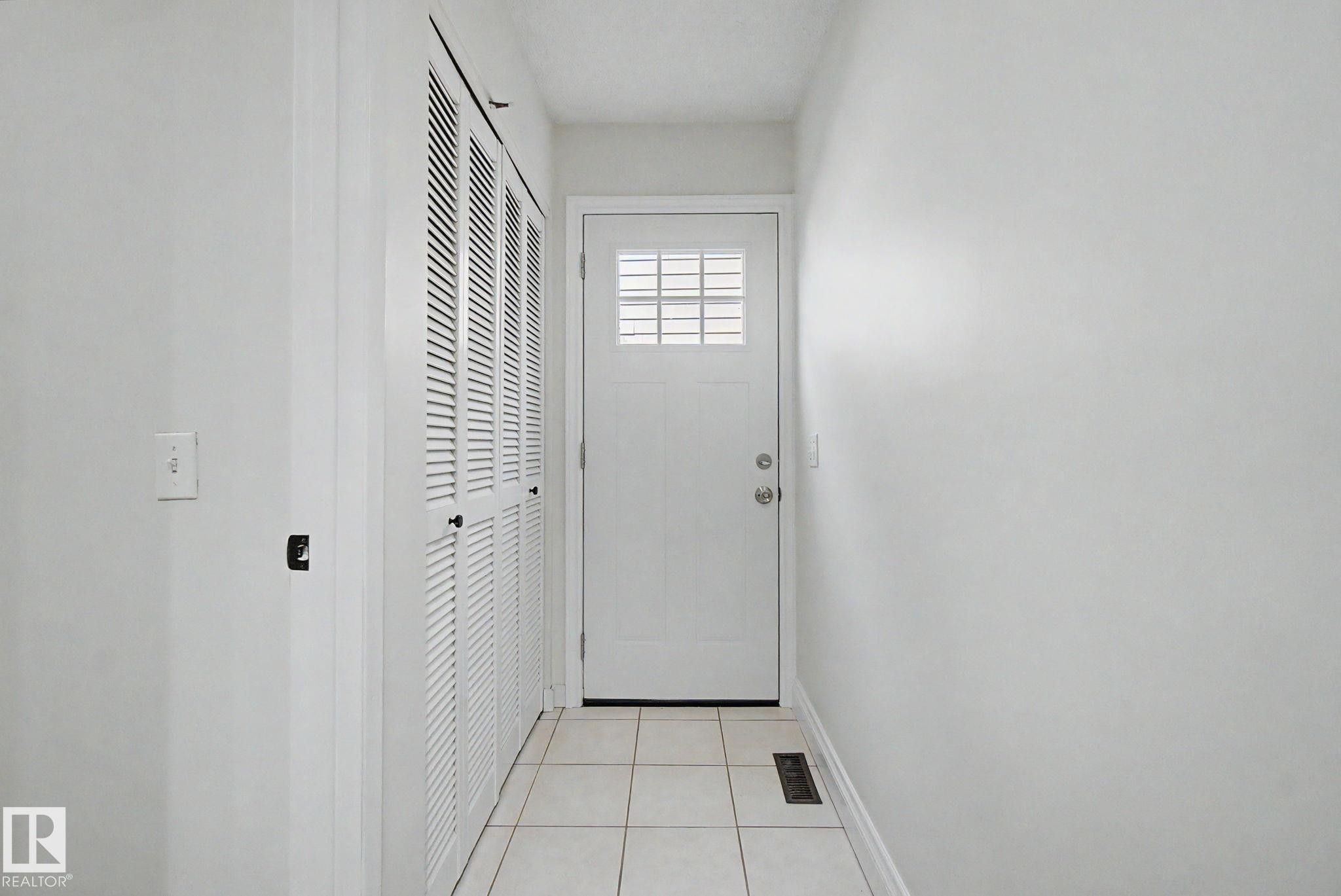 Entryway featuring a paneled door with grid window insert, louvered bi-fold doors, white ceramic tile flooring, and white painted walls - 170 Westridge Rd, Edmonton, AB - Indoor Photo Showing Other Room
