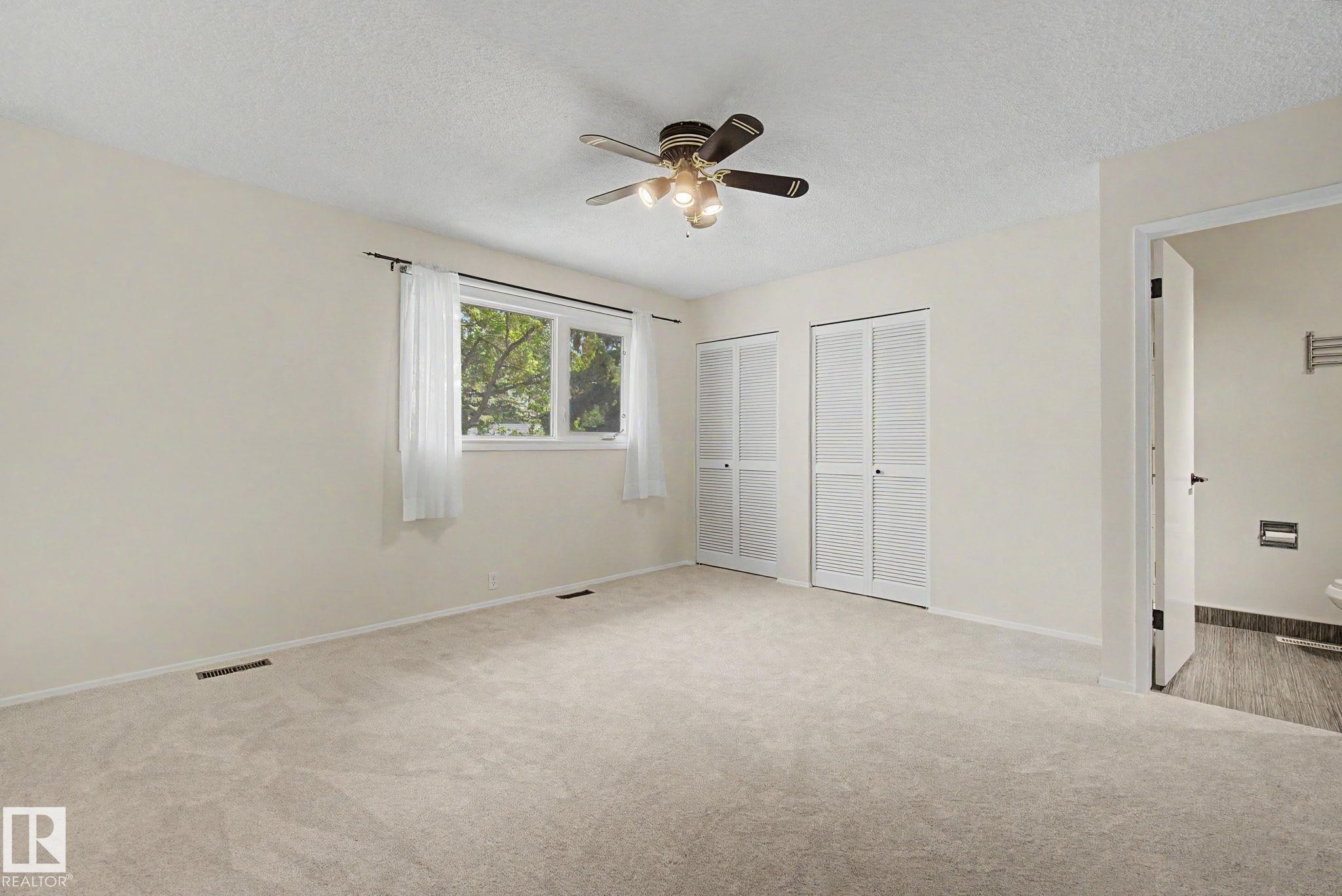Spacious room featuring neutral carpeting, a large window, two bi-fold louvered closets, a ceiling fan with integrated lighting, and direct access to a separate area with dark-toned floor tiling - 170 Westridge Rd, Edmonton, AB - Indoor Photo Showing Other Room