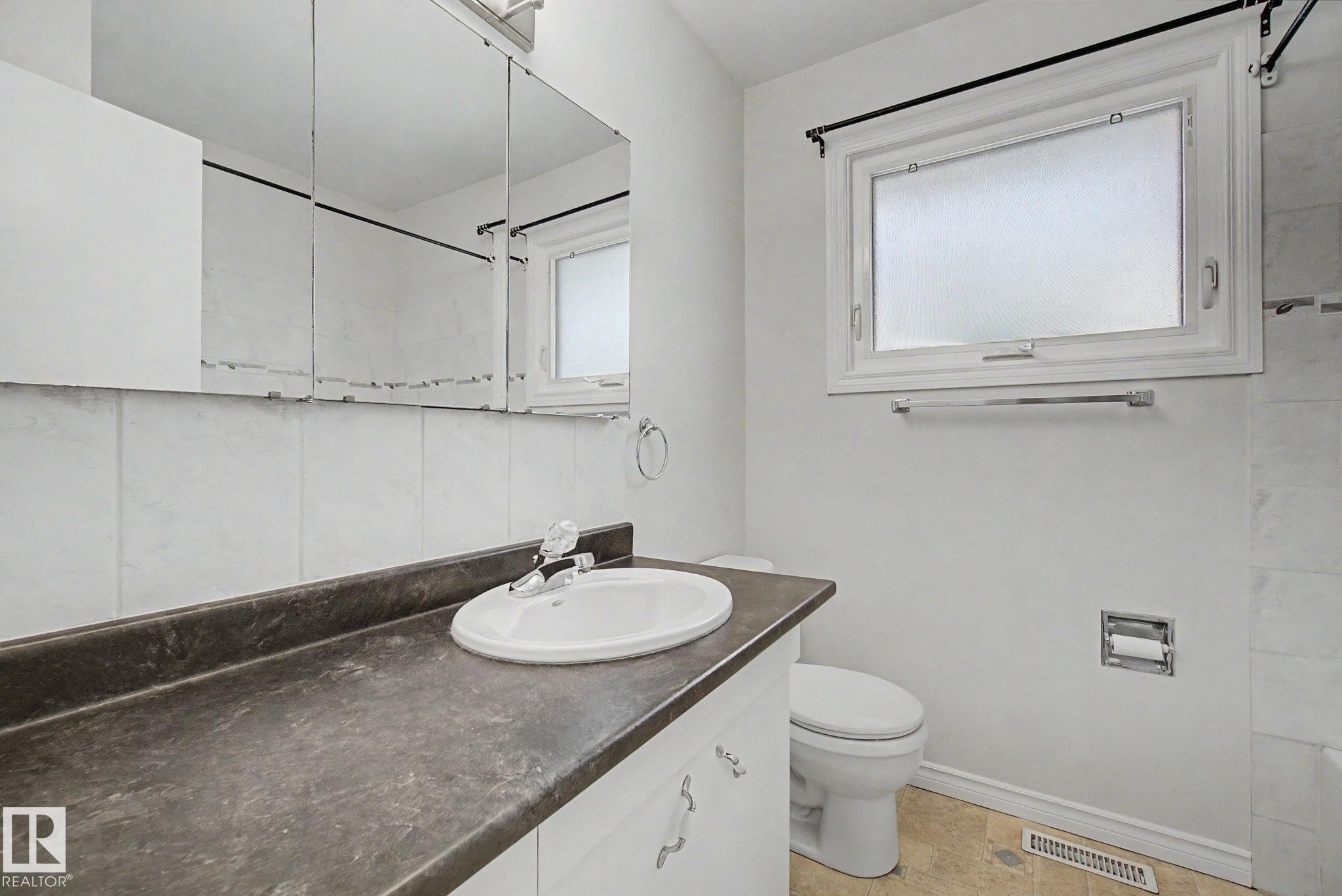 Bathroom vanity featuring an integrated sink, dark countertop, and white cabinetry - 170 Westridge Rd, Edmonton, AB - Indoor Photo Showing Bathroom
