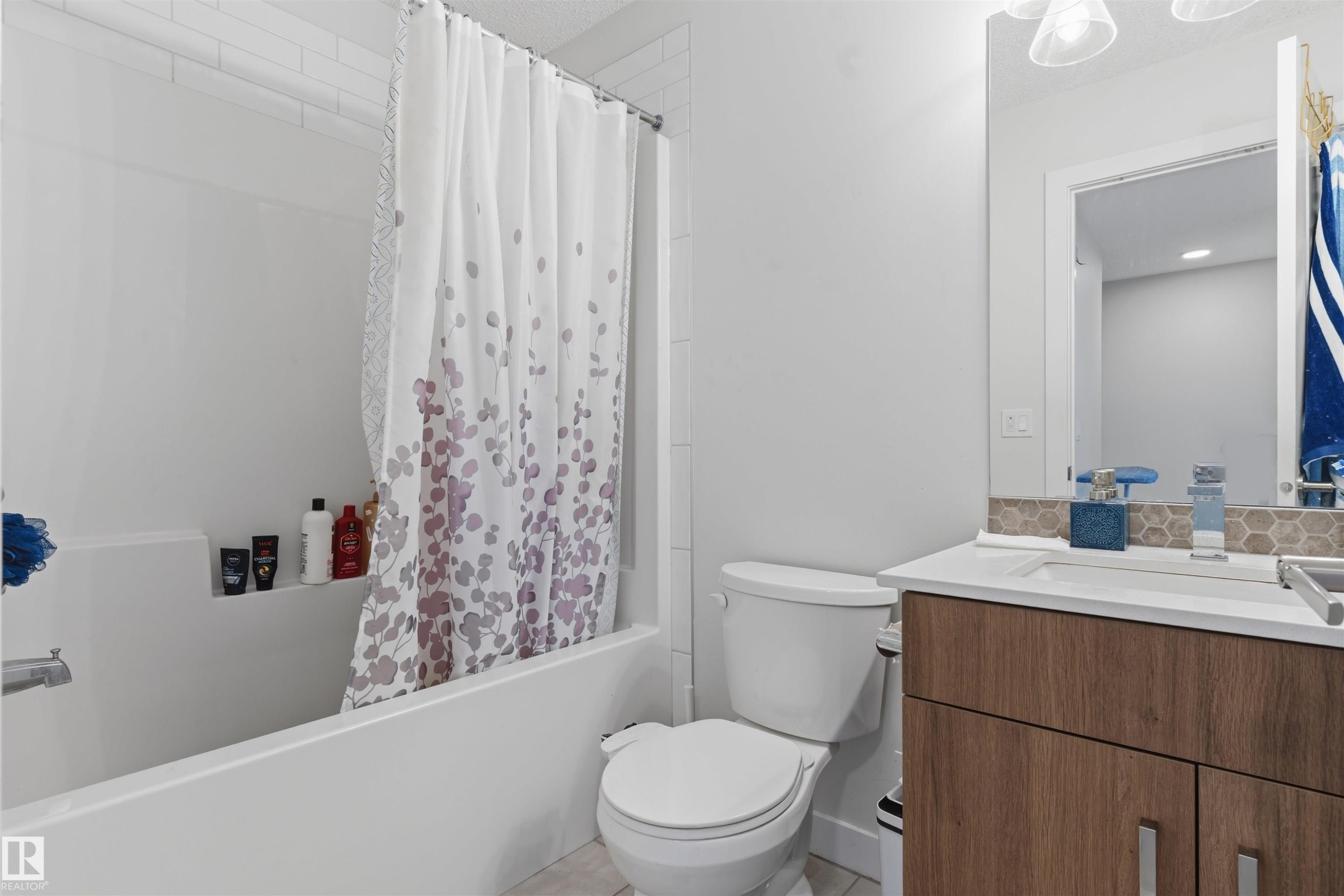 Bathroom featuring a white subway tile shower surround, a built-in tub with shelf, a floating wood-finish vanity with an undermount sink, and a hexagonal tile backsplash - 170 804 Welsh Drive, Edmonton, AB