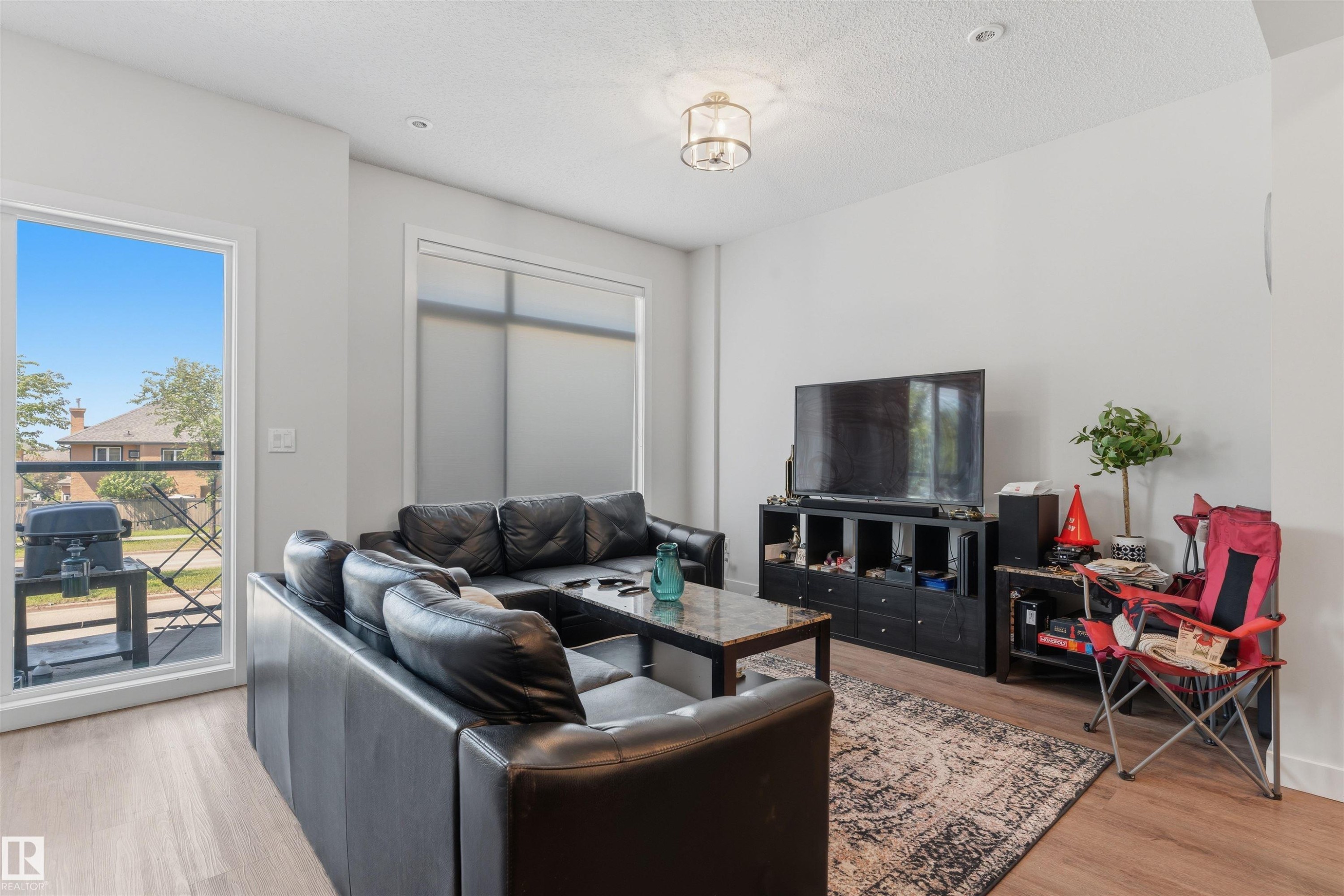 Bright living area featuring wood-finish flooring, a large window with a balcony, and a recessed ceiling light - 170 804 Welsh Drive, Edmonton, AB