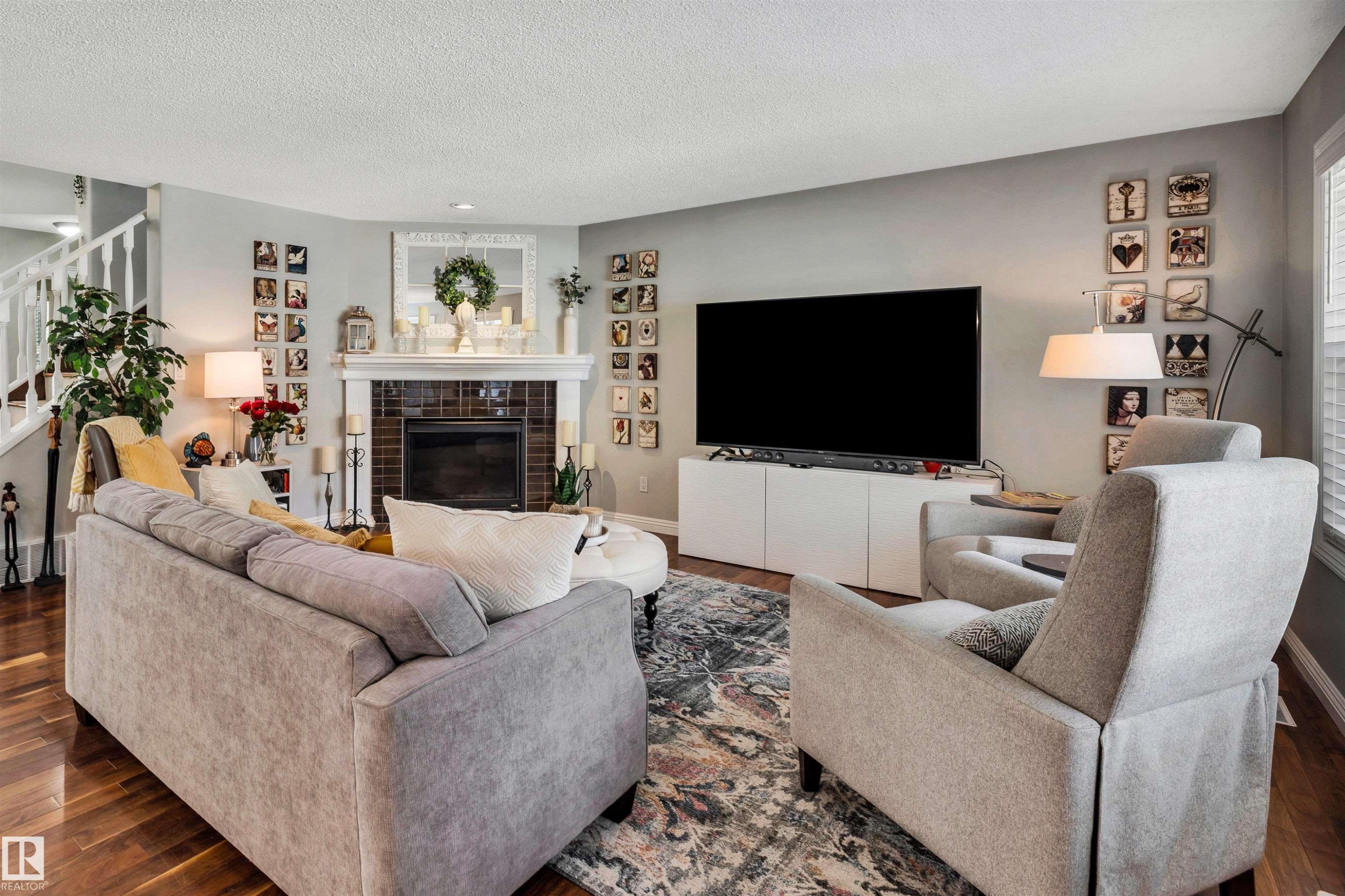 Spacious living area featuring rich wood-finish flooring, a traditional fireplace with a white mantel and tiled surround, and a white open-spindle staircase - 9804 145 Avenue, Edmonton, AB