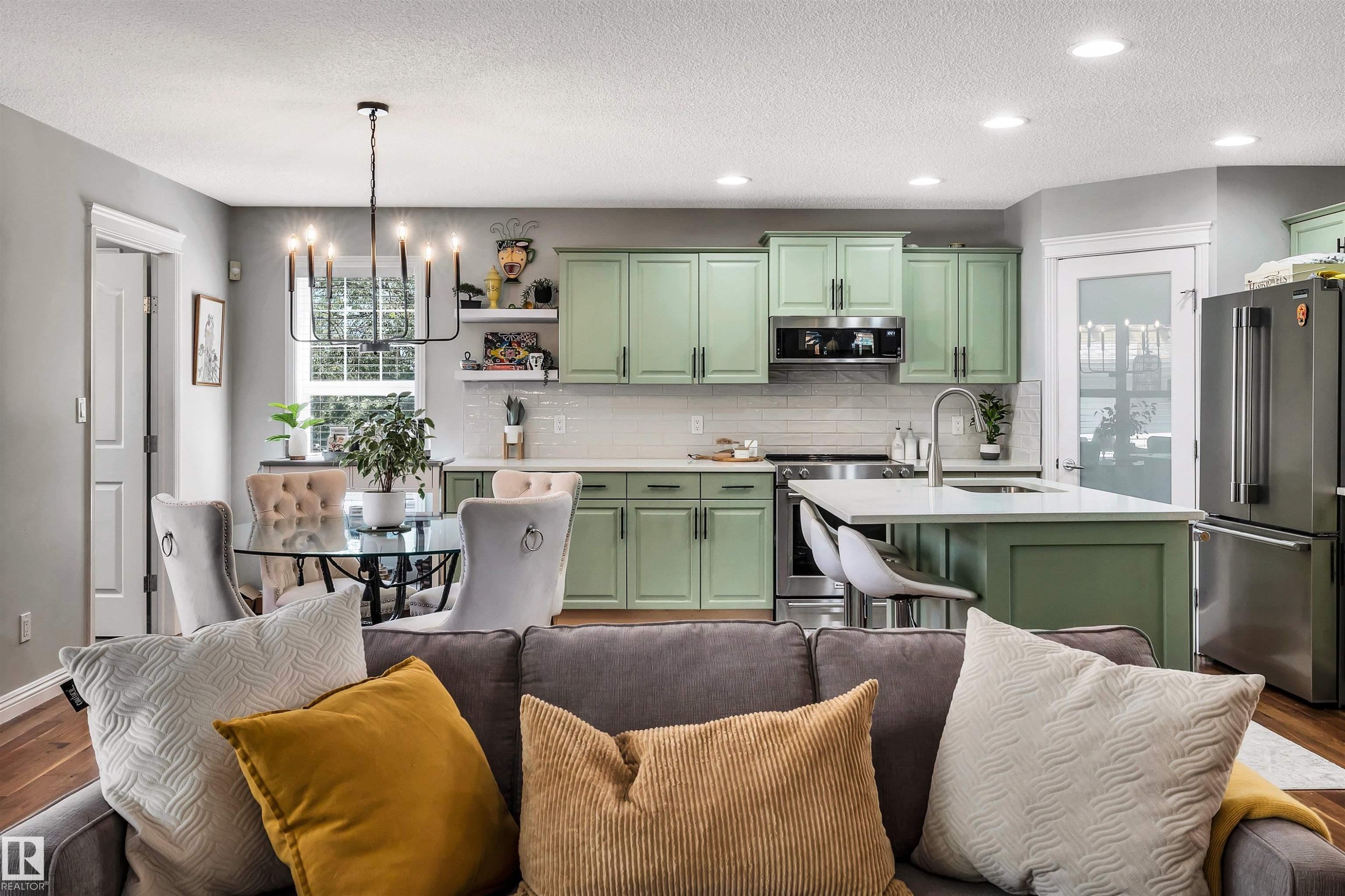 Open-concept living space featuring a kitchen with custom-colored cabinetry, stainless steel appliances, and a central island with bar seating - 9804 145 Avenue, Edmonton, AB