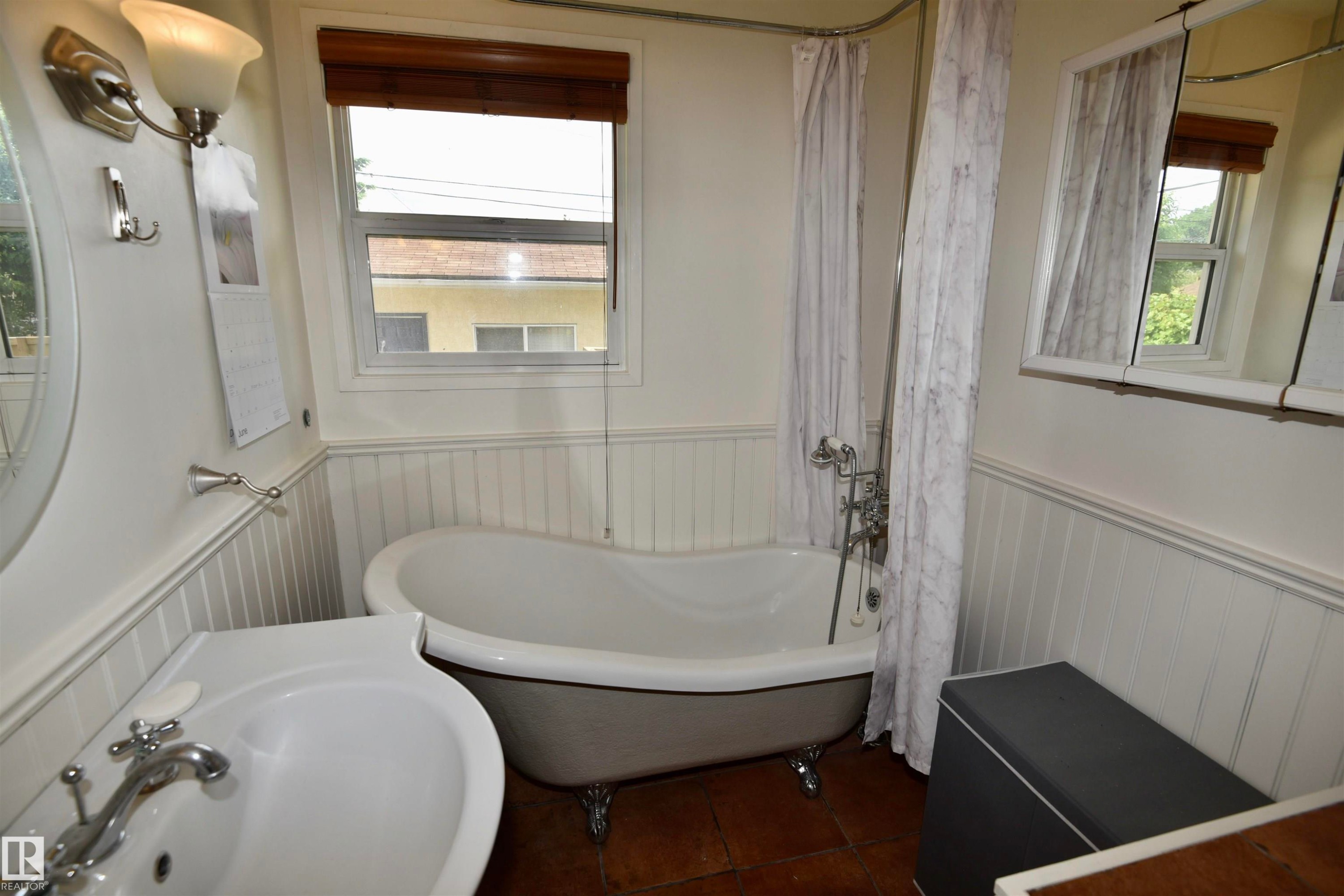 Bathroom featuring a white clawfoot tub with shower attachment, single vanity with integrated sink, white beadboard wainscoting, and wood-finish flooring - 7923 94 Avenue Nw, Edmonton, AB - Indoor Photo Showing Bathroom