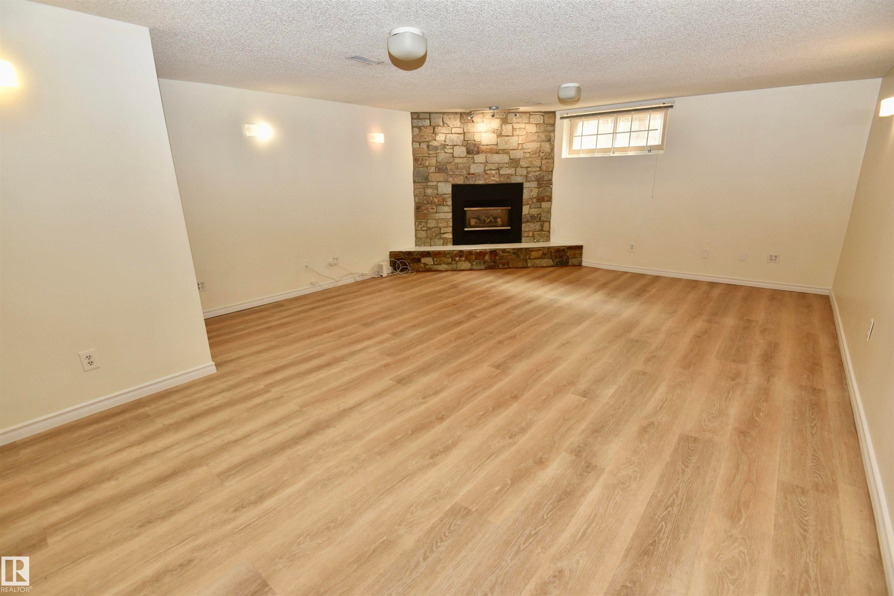Spacious room featuring wood-finish flooring and a stone-clad fireplace - 7923 94 Avenue Nw, Edmonton, AB - Indoor Photo Showing Living Room With Fireplace