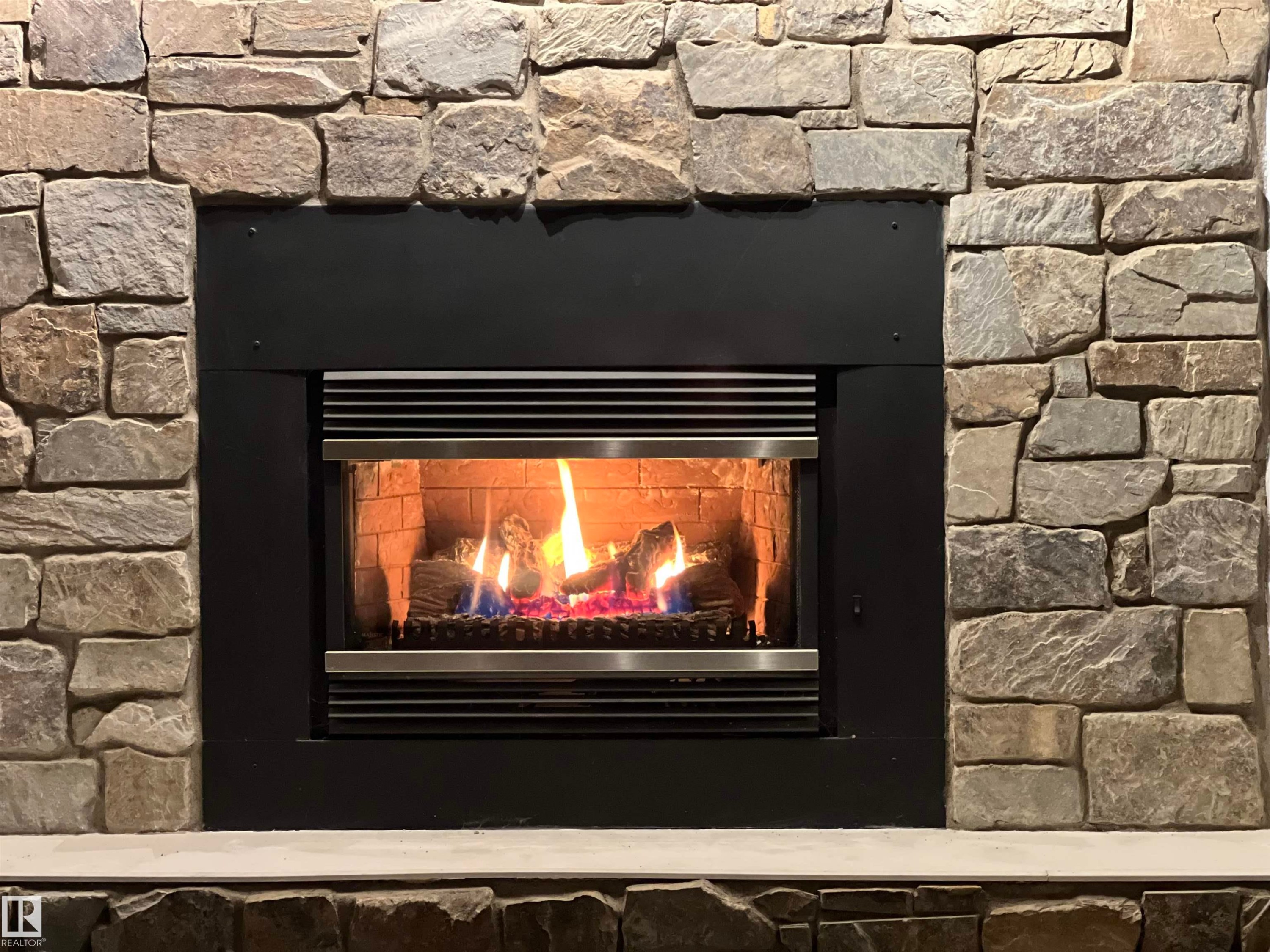 Stone-clad fireplace with a modern black inset firebox and a light-colored hearth - 7923 94 Avenue Nw, Edmonton, AB - Indoor