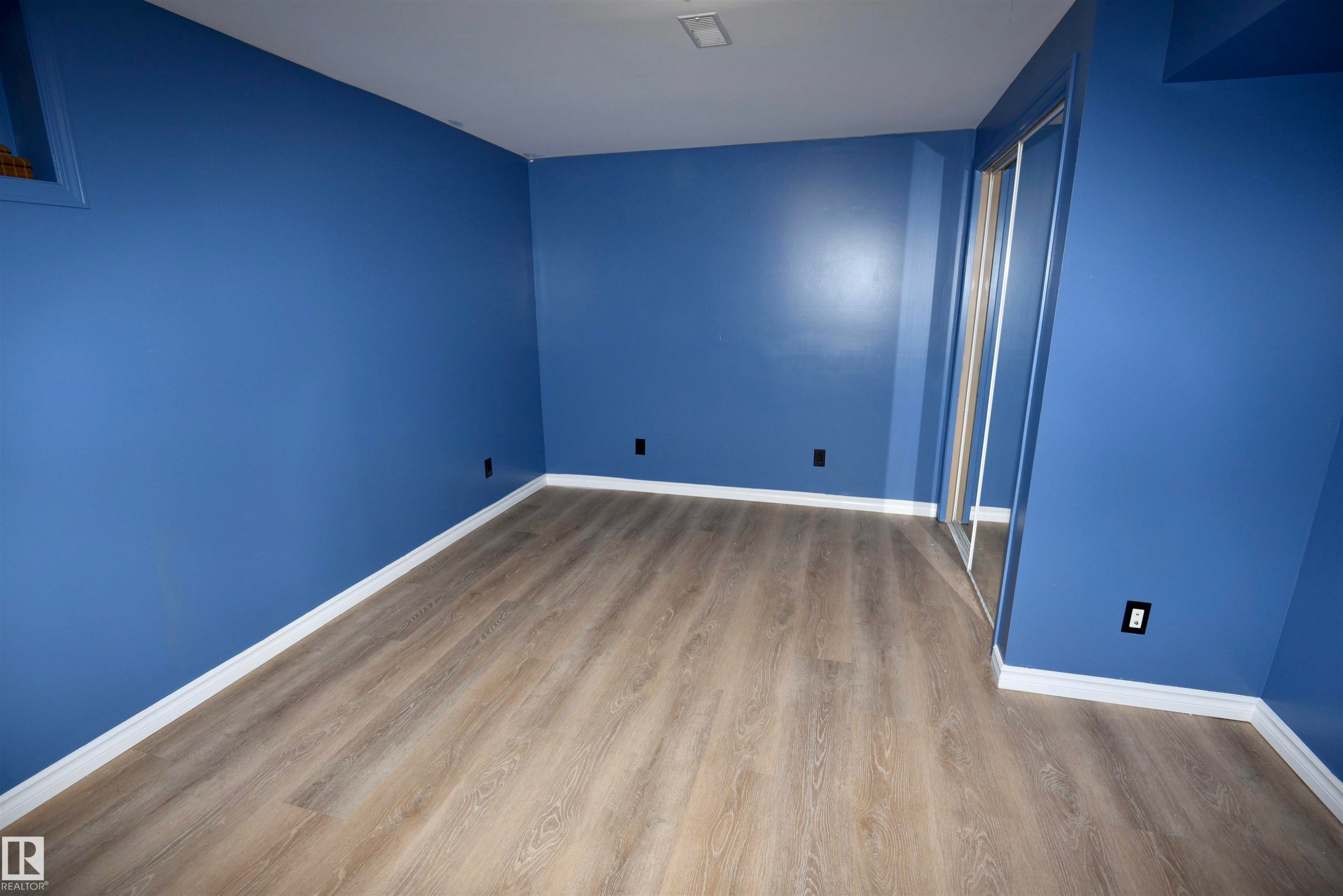 Room featuring wood-finish flooring, white baseboards, and a mirrored closet door - 7923 94 Avenue Nw, Edmonton, AB - Indoor Photo Showing Other Room