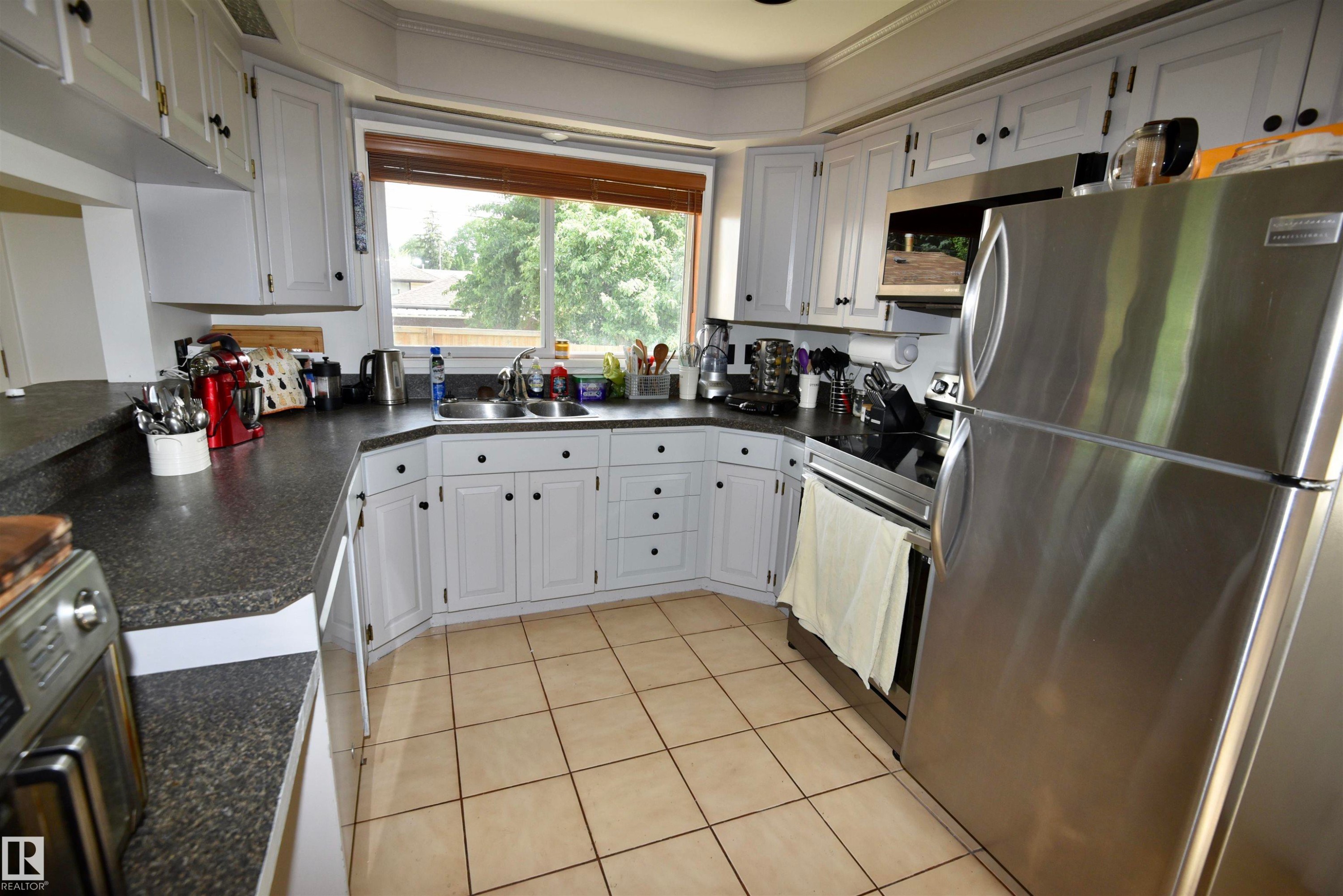 Kitchen featuring light-toned cabinetry with dark hardware, dark countertops, and stainless steel appliances - 7923 94 Avenue Nw, Edmonton, AB - Indoor Photo Showing Kitchen With Stainless Steel Kitchen With Double Sink