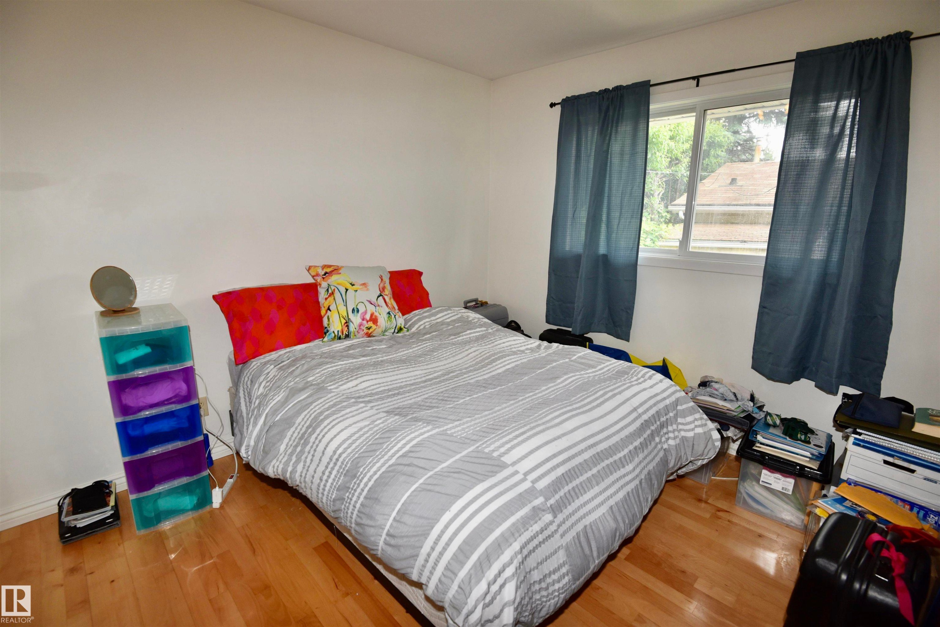 Bedroom featuring wood-finish flooring, white painted walls, and a large window with blue curtains - 7923 94 Avenue Nw, Edmonton, AB - Indoor Photo Showing Bedroom