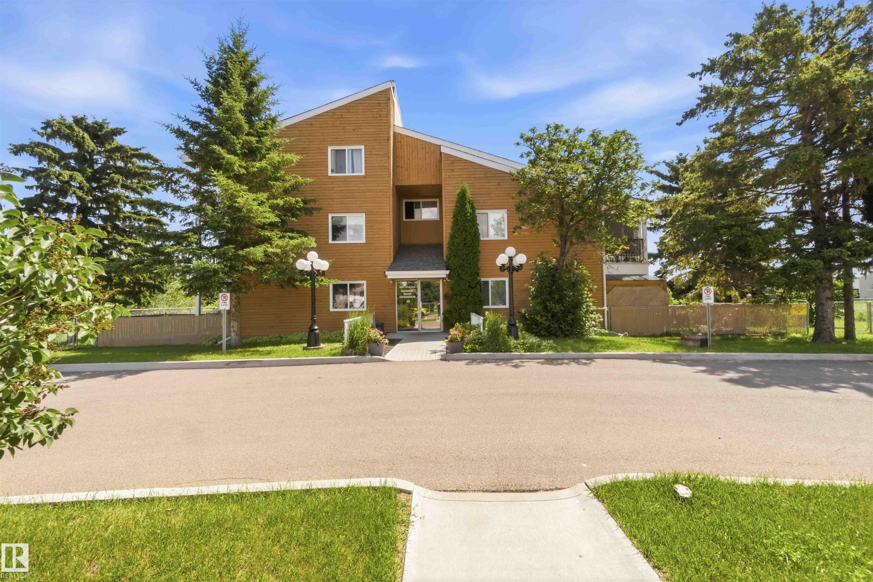 Three-story residential building with wood-finish siding, multiple windows, and a central entrance - 204 4601 131 Avenue, Edmonton, AB