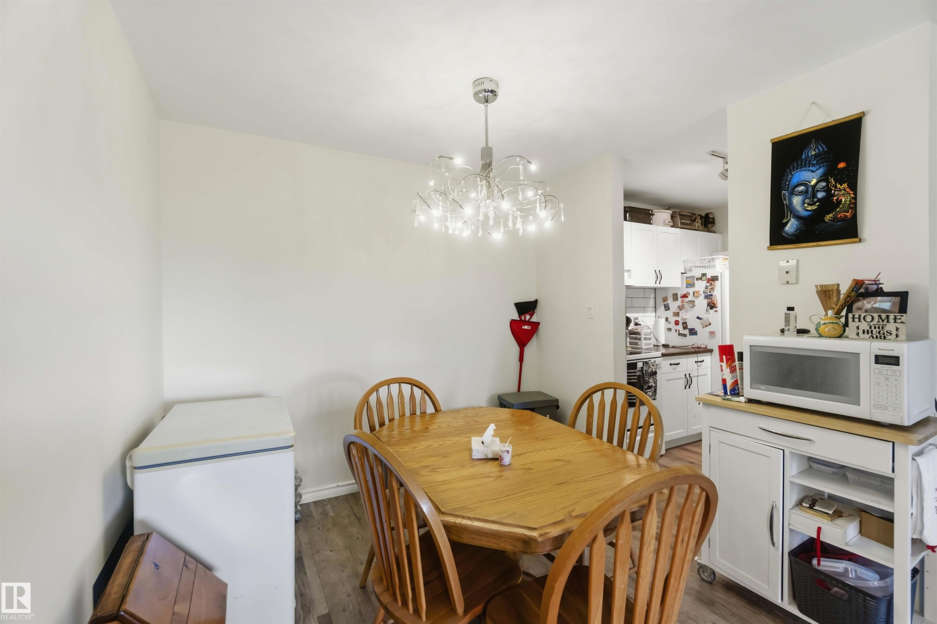 Dining area featuring wood-finish flooring, a modern chandelier, and neutral wall tones - 204 4601 131 Avenue, Edmonton, AB