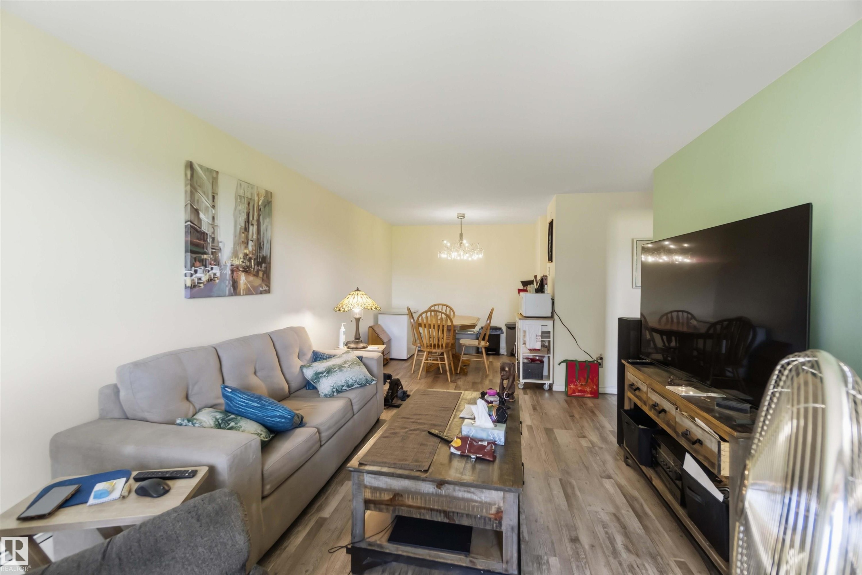 Open-concept living space featuring wood-finish flooring, a light-toned ceiling, and a dining area with a chandelier - 204 4601 131 Avenue, Edmonton, AB
