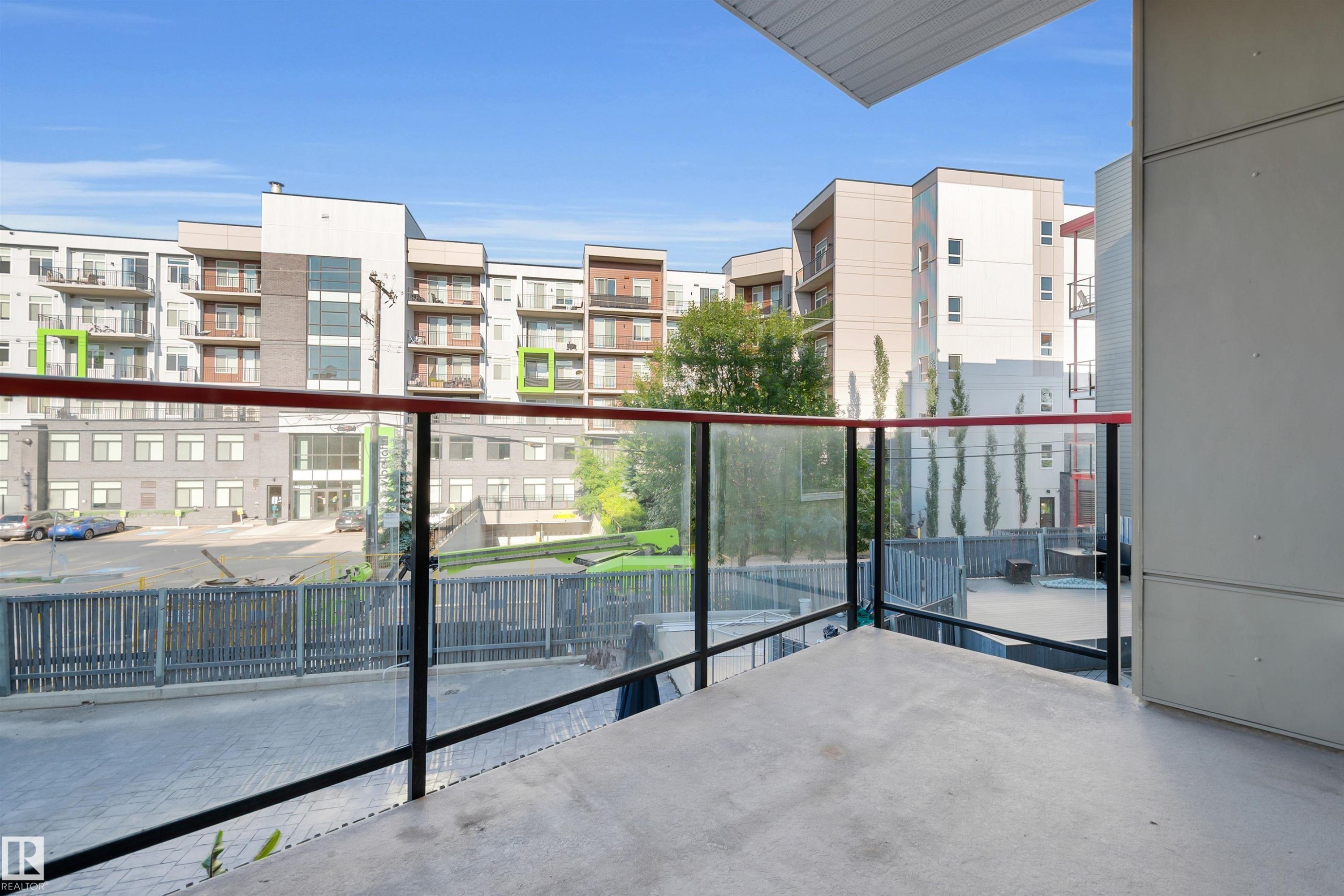Private balcony with concrete flooring, glass railing, and red handrail accents - #209 10611 117 St Nw, Edmonton, AB - Outdoor With Balcony With Exterior