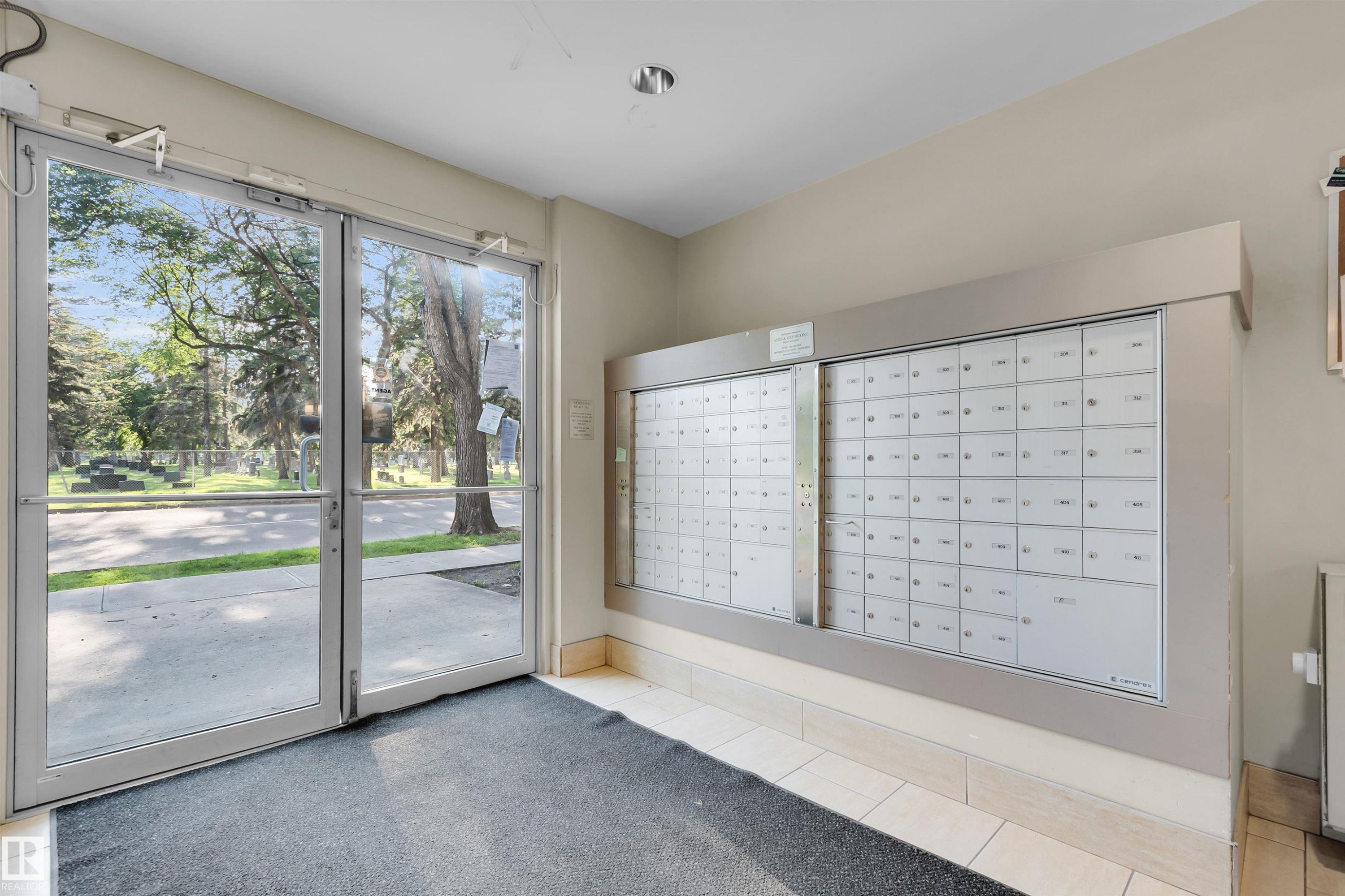 Entry vestibule featuring a wall of individual mailboxes, dual glass entry doors, and overhead lighting - #209 10611 117 St Nw, Edmonton, AB - Indoor Photo Showing Other Room