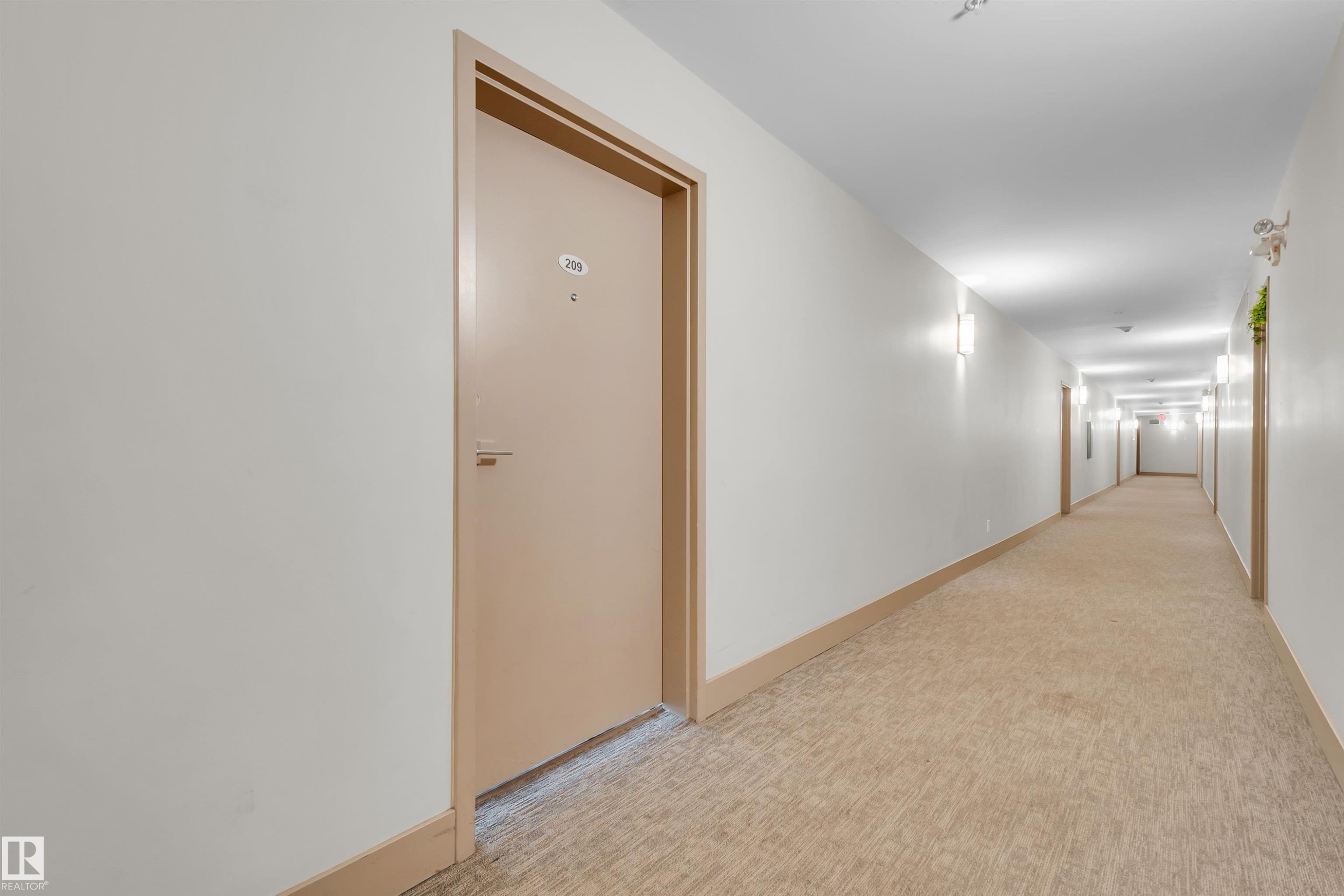 Corridor featuring light-colored carpeting, white walls, and warm-toned wall sconces - #209 10611 117 St Nw, Edmonton, AB - Indoor Photo Showing Other Room