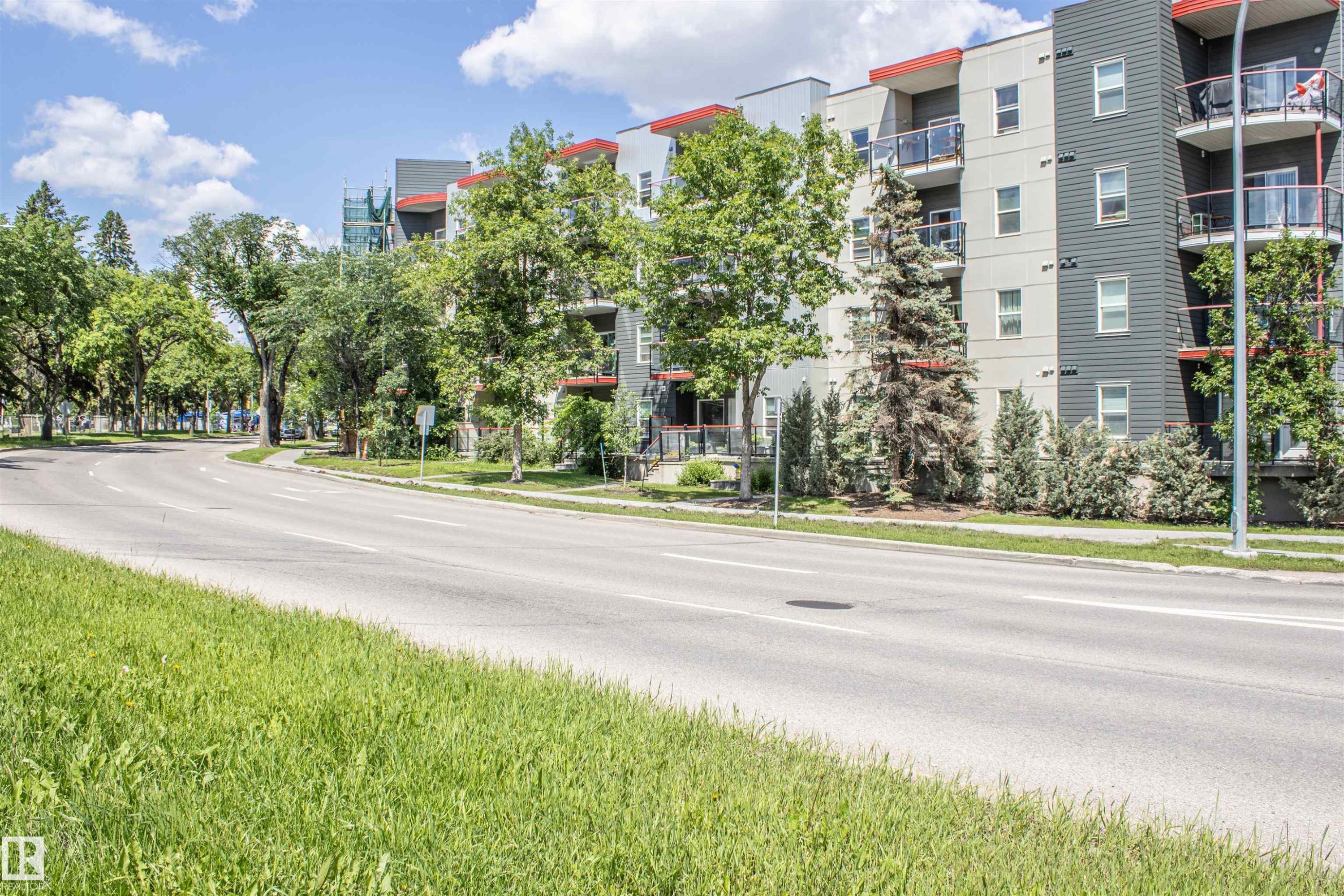 Modern multi-story building featuring grey and white exterior siding with red accent trim - #209 10611 117 St Nw, Edmonton, AB - Outdoor With Balcony