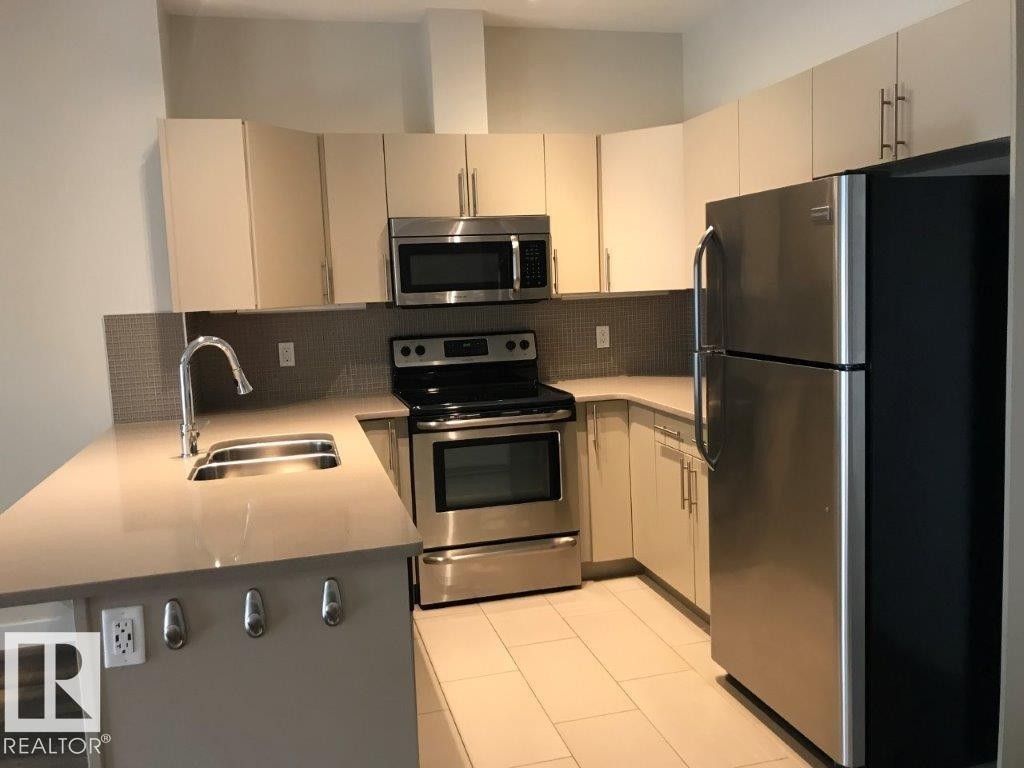 Modern kitchen featuring a U-shaped layout with light-toned cabinetry and stainless steel appliances - #209 10611 117 St Nw, Edmonton, AB