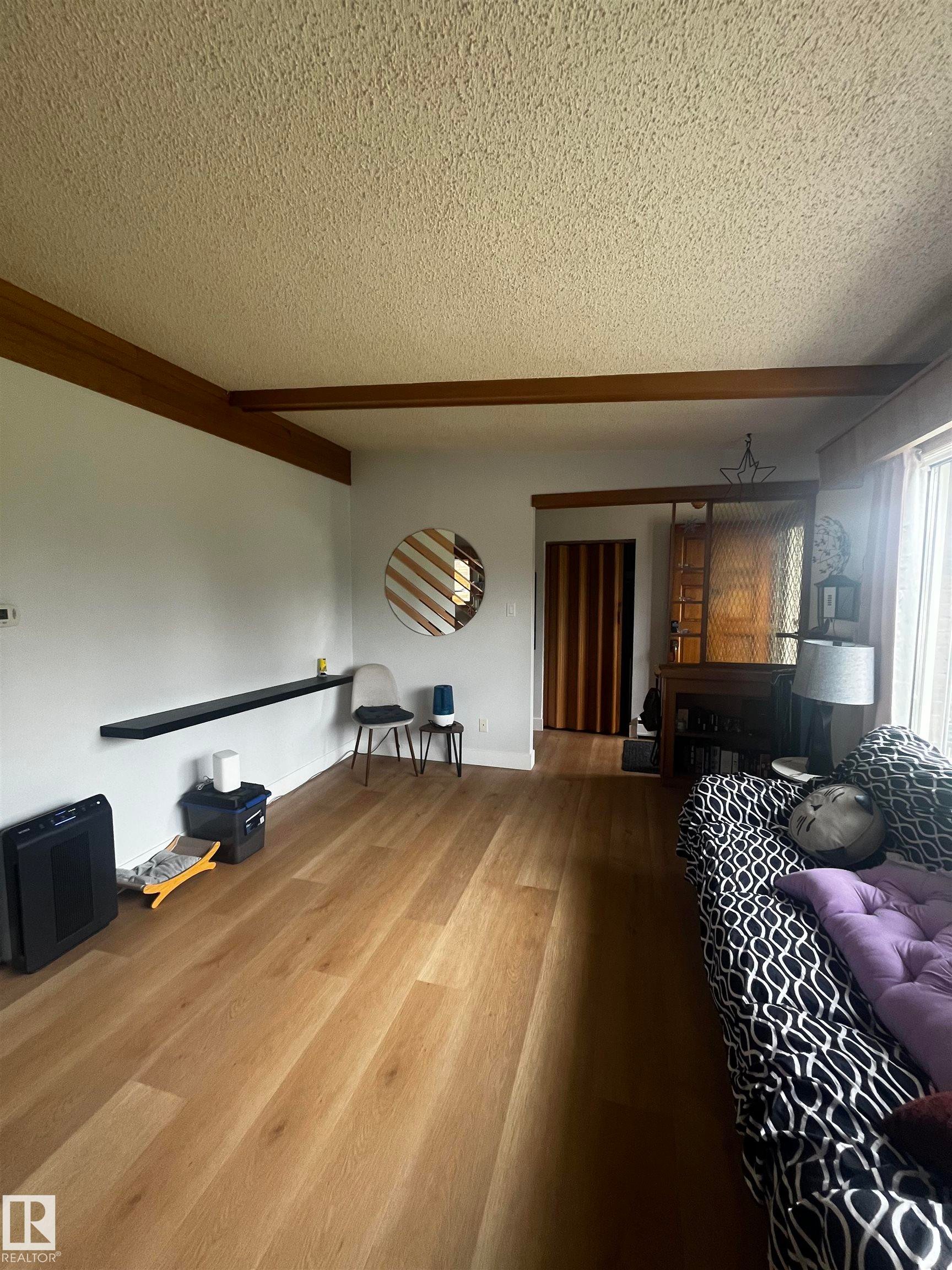 Spacious room featuring wood-finish flooring, white walls, and a textured ceiling - 8736 72 Street Nw, Edmonton, AB - Indoor