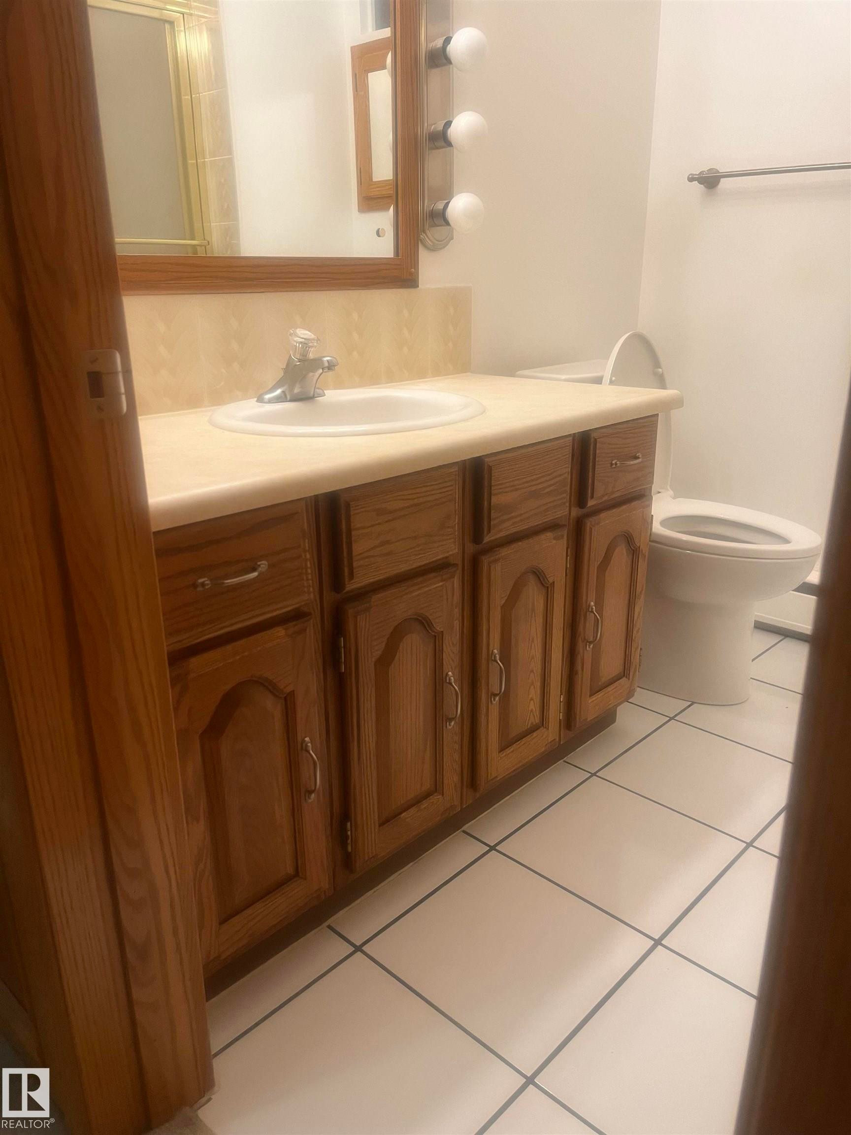 Bathroom vanity featuring wood-finish cabinetry with silver-tone hardware, an integrated white sink, and a light-toned countertop with matching backsplash - 8736 72 Street Nw, Edmonton, AB - Indoor Photo Showing Bathroom