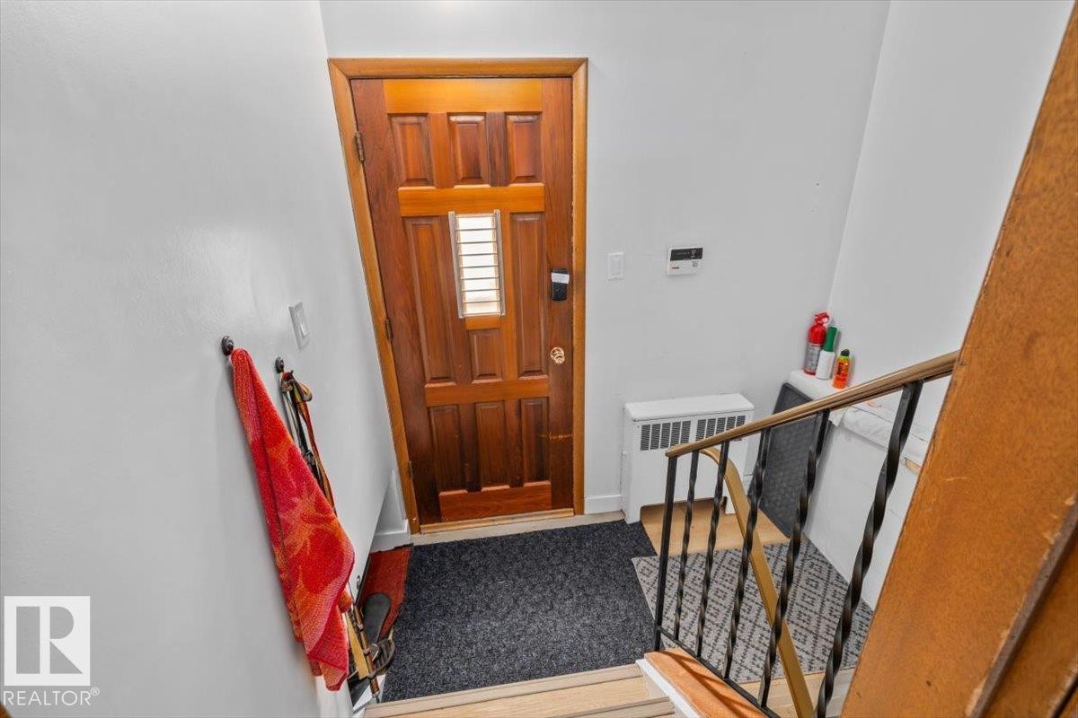Wood-paneled entry door with frosted glass insert, black metal stair railing, and white wall finishes - 8736 72 Street Nw, Edmonton, AB - Indoor Photo Showing Other Room