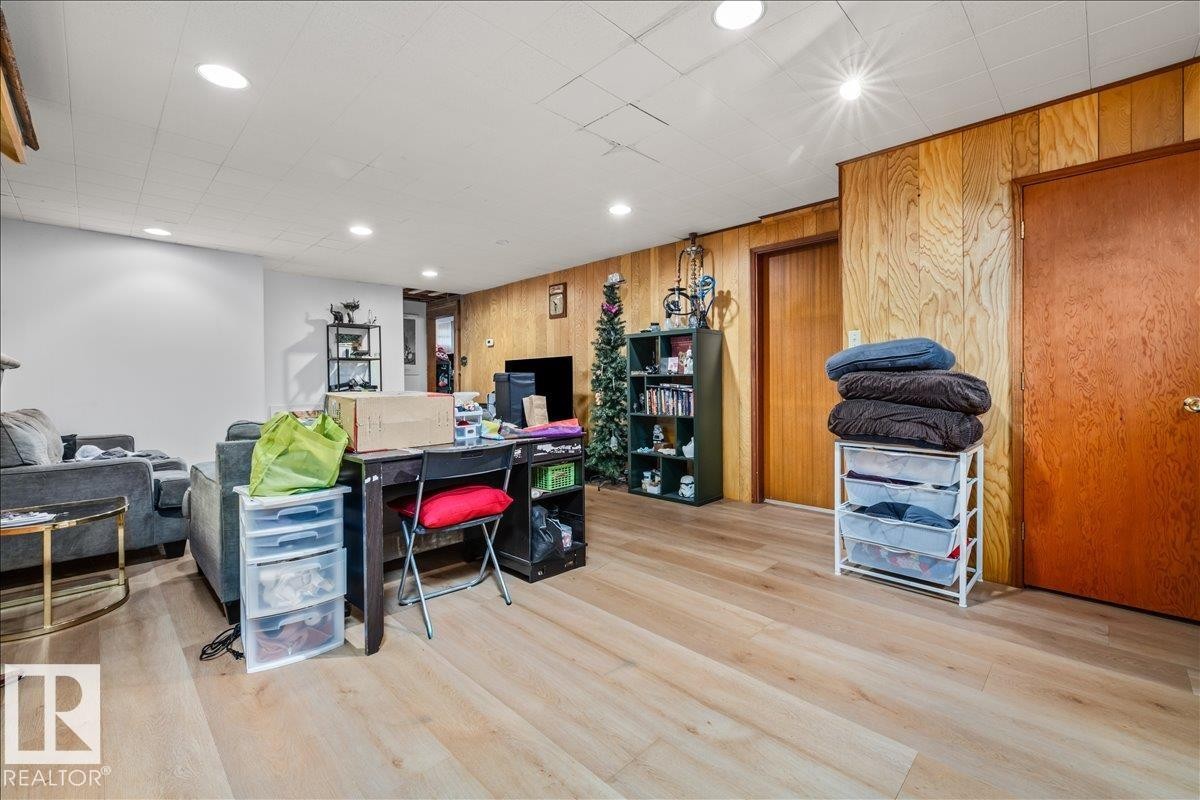 Spacious room featuring light wood-finish flooring, recessed ceiling lighting, and a combination of white painted walls and wood paneling - 8736 72 Street Nw, Edmonton, AB - Indoor