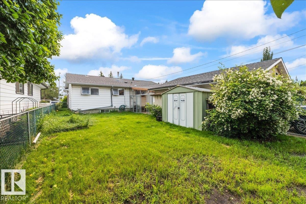 Expansive grassy yard area featuring a chain link fence, mature trees, and an exterior storage shed - 8736 72 Street Nw, Edmonton, AB - Outdoor