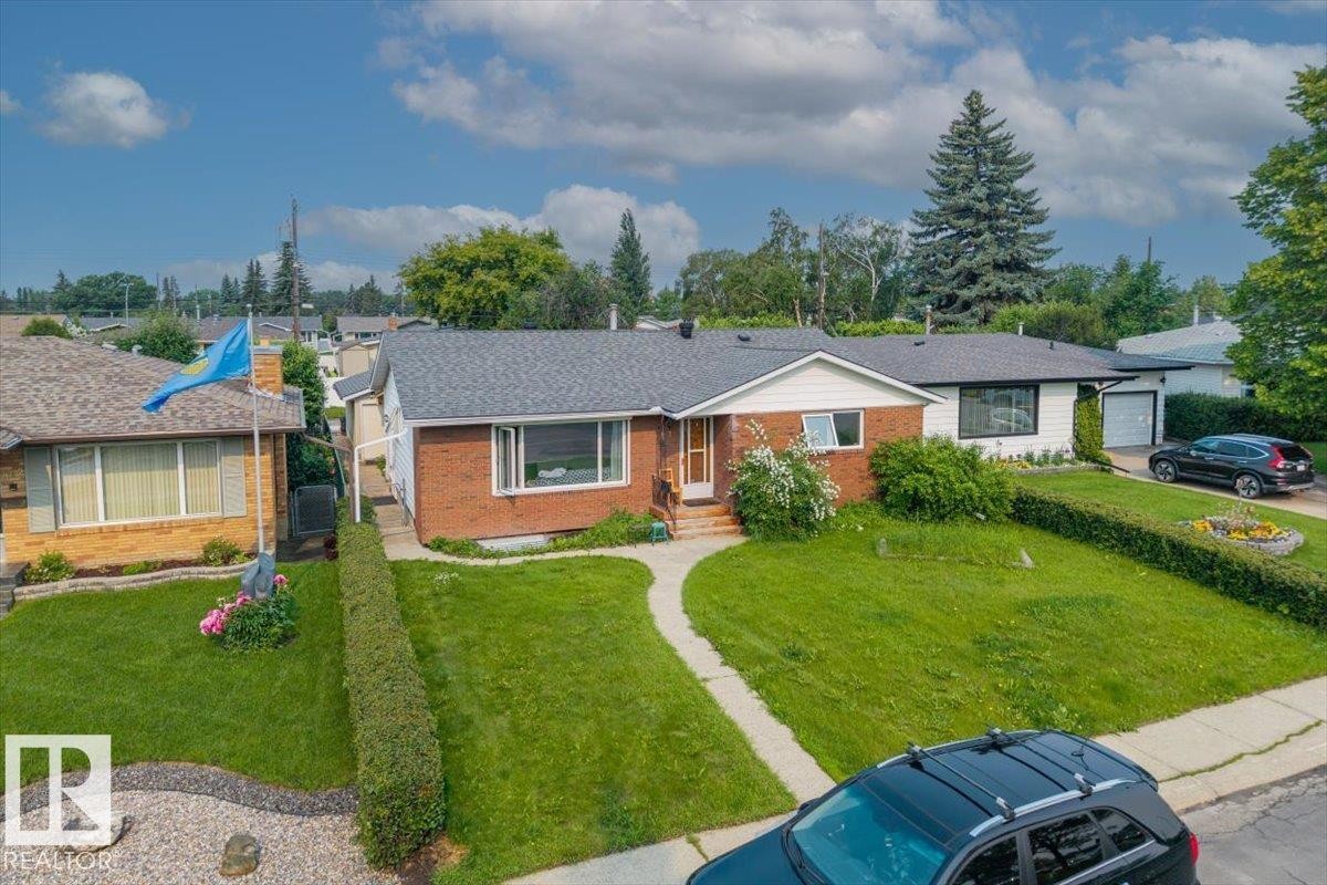Brick facade home with a dark shingle roof, featuring a front lawn with a concrete walkway, established shrubs, and a paved driveway leading to an attached garage - 8736 72 Street Nw, Edmonton, AB - Outdoor With Facade