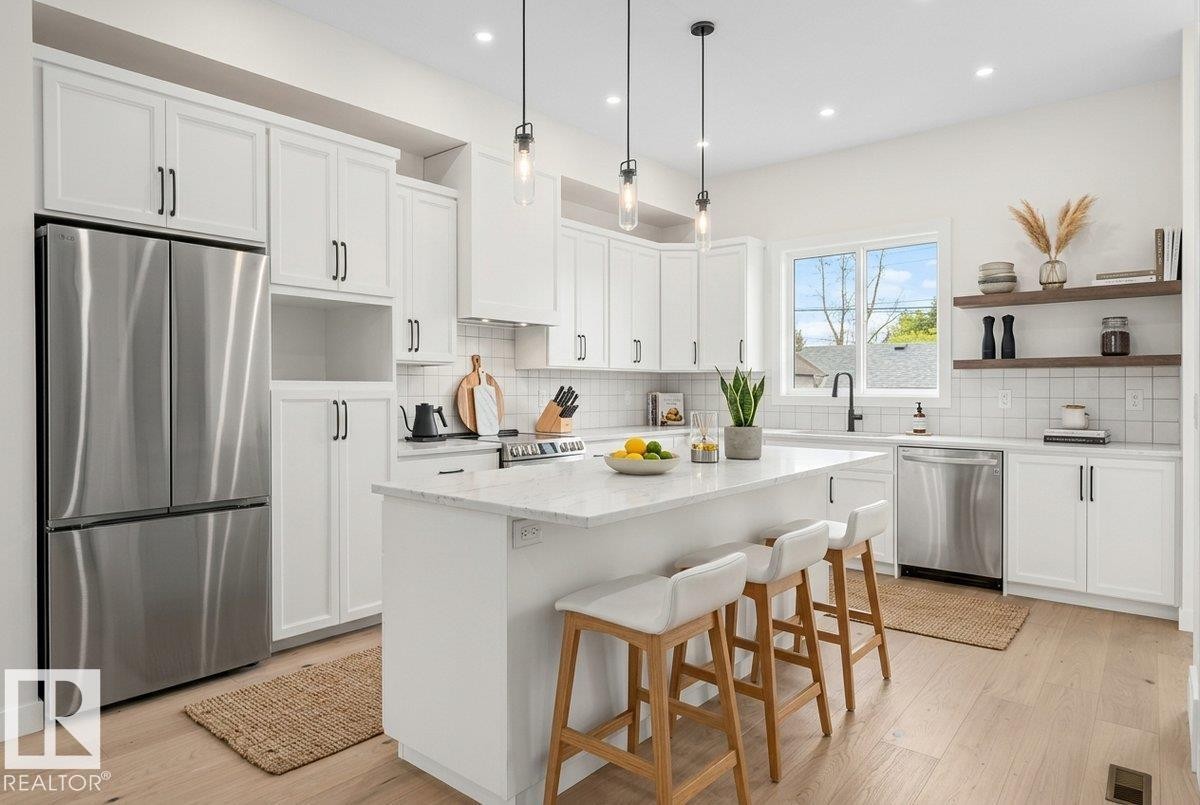 Bright kitchen featuring white shaker cabinetry, stainless steel appliances, a center island with countertop seating, wood-finish flooring, and pendant lighting - 10934 132 Street, Edmonton, AB - Indoor Photo Showing Kitchen With Upgraded Kitchen