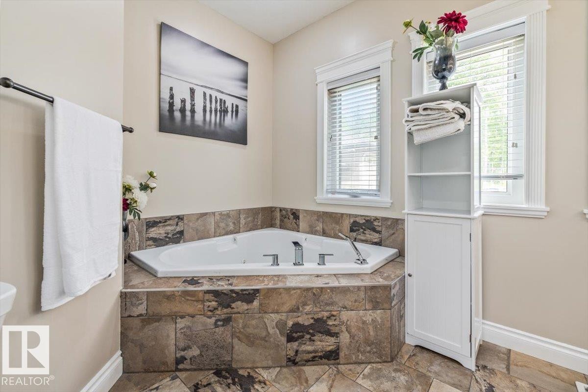 Corner jetted tub set within a natural stone tile surround, complemented by a matching stone tile floor - #6 2406 Twp Road 540, Rural Lac Ste. Anne County, AB - Indoor Photo Showing Bathroom