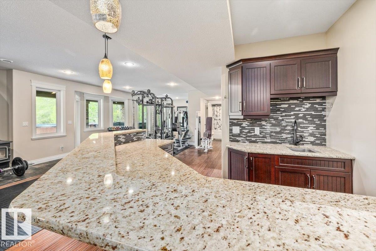 Expansive stone-finish countertop bar with a built-in sink and dark wood-finish cabinetry - #6 2406 Twp Road 540, Rural Lac Ste. Anne County, AB - Indoor Photo Showing Kitchen