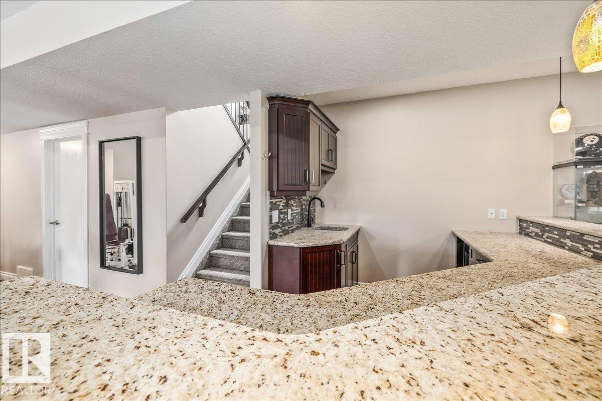 Expansive granite countertop bar area featuring a built-in wet bar with dark wood cabinetry, a contemporary black faucet, and a mosaic tile backsplash - #6 2406 Twp Road 540, Rural Lac Ste. Anne County, AB - Indoor