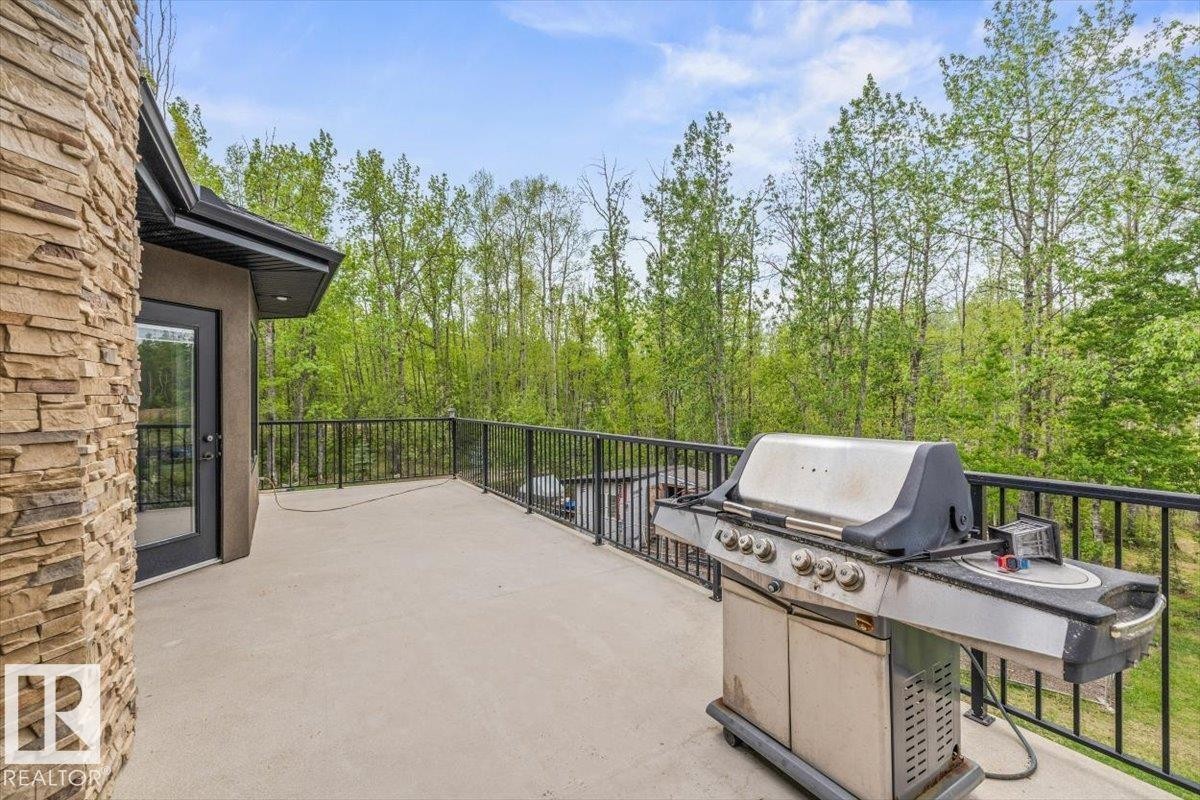 Expansive exterior deck featuring a stone facade, glass-paneled door, and black metal railing, surrounded by mature trees - #6 2406 Twp Road 540, Rural Lac Ste. Anne County, AB - Outdoor With Exterior