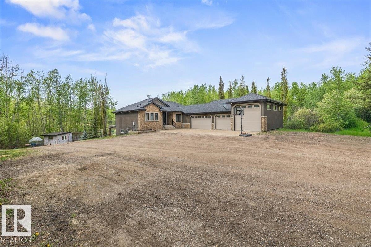 Two-story residential structure featuring a stone and siding exterior, a multi-car garage with three overhead doors, and a dark shingled roof - #6 2406 Twp Road 540, Rural Lac Ste. Anne County, AB - Outdoor