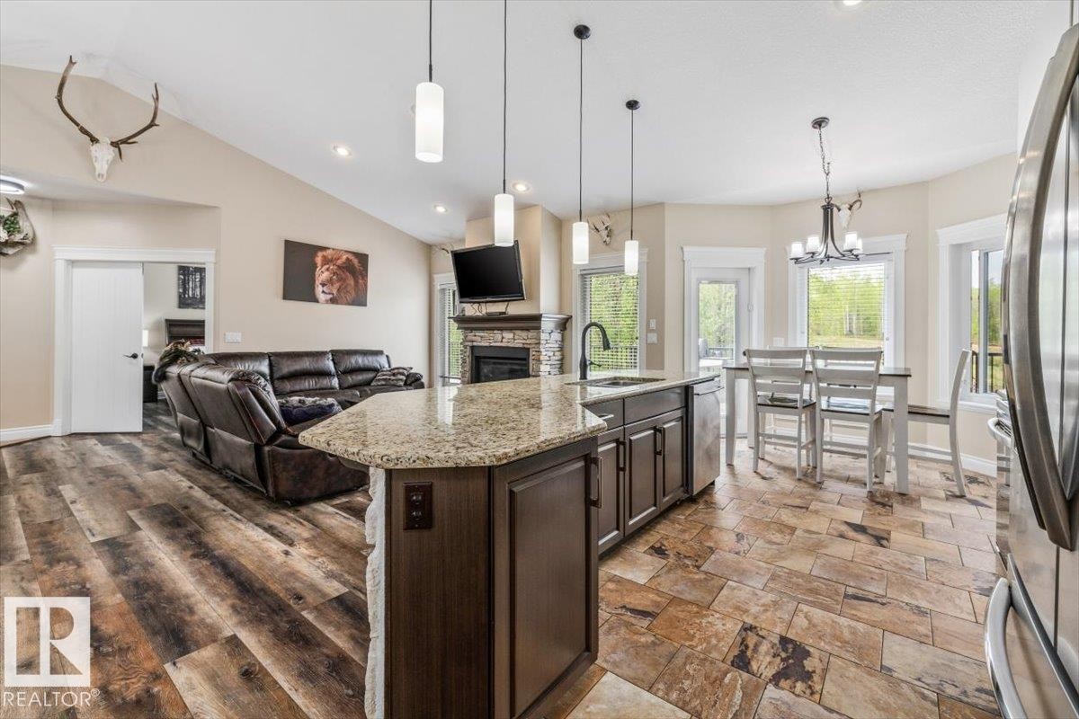 Open-concept living space featuring vaulted ceilings, wood-finish flooring, a stone-faced fireplace, a kitchen island with granite countertop, and natural light from multiple windows - #6 2406 Twp Road 540, Rural Lac Ste. Anne County, AB - Indoor Photo Showing Kitchen With Upgraded Kitchen