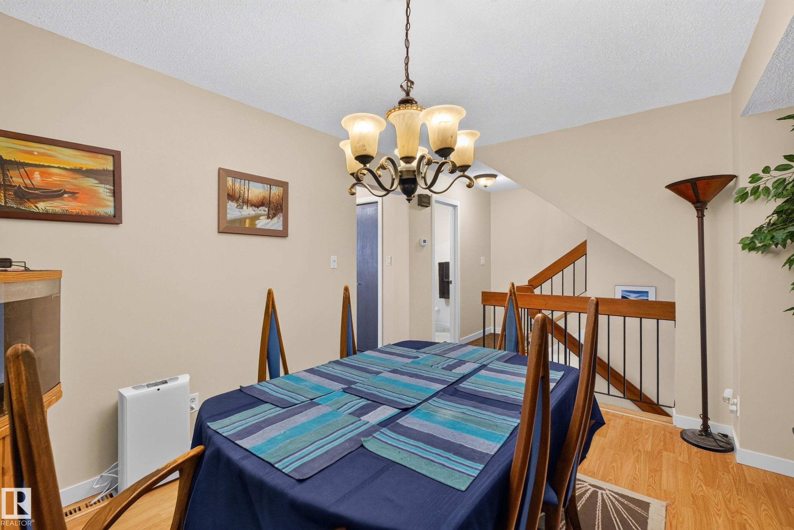 Dining area with a multi-arm chandelier, wood-finish flooring, and a stairway featuring a wood handrail and black metal spindles - 12062 157 Avenue, Edmonton, AB