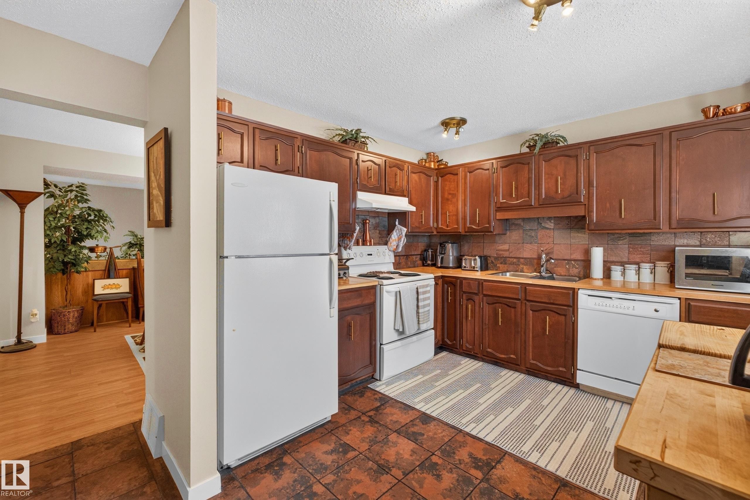 Kitchen featuring wood cabinetry, white appliances, a brick-style tile backsplash, and tile flooring - 12062 157 Avenue, Edmonton, AB