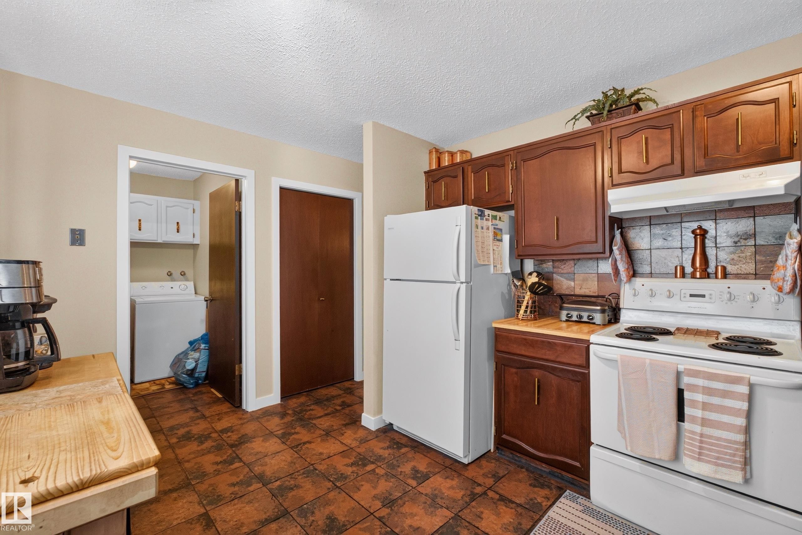 Kitchen featuring wood-finish cabinetry, tile backsplash, and white appliances - 12062 157 Avenue, Edmonton, AB