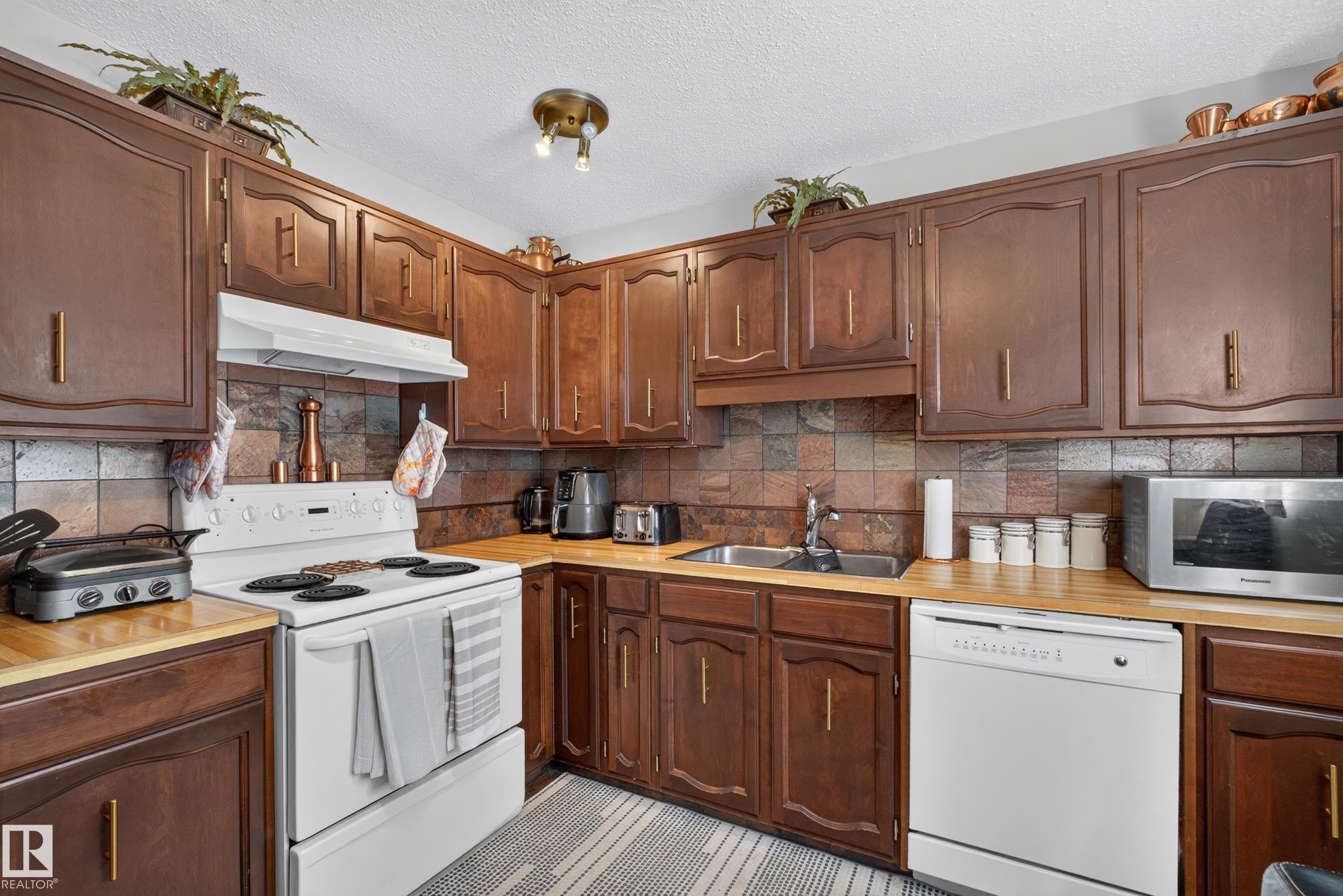 Kitchen with wood-finish cabinetry, butcher block style countertops, and a full suite of white appliances including a range, hood, and dishwasher - 12062 157 Avenue, Edmonton, AB