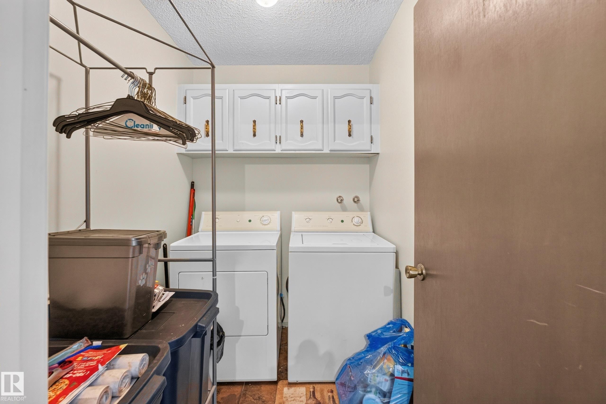 Dedicated laundry area featuring a washer and dryer, wood-finish flooring, and upper cabinetry for storage - 12062 157 Avenue, Edmonton, AB