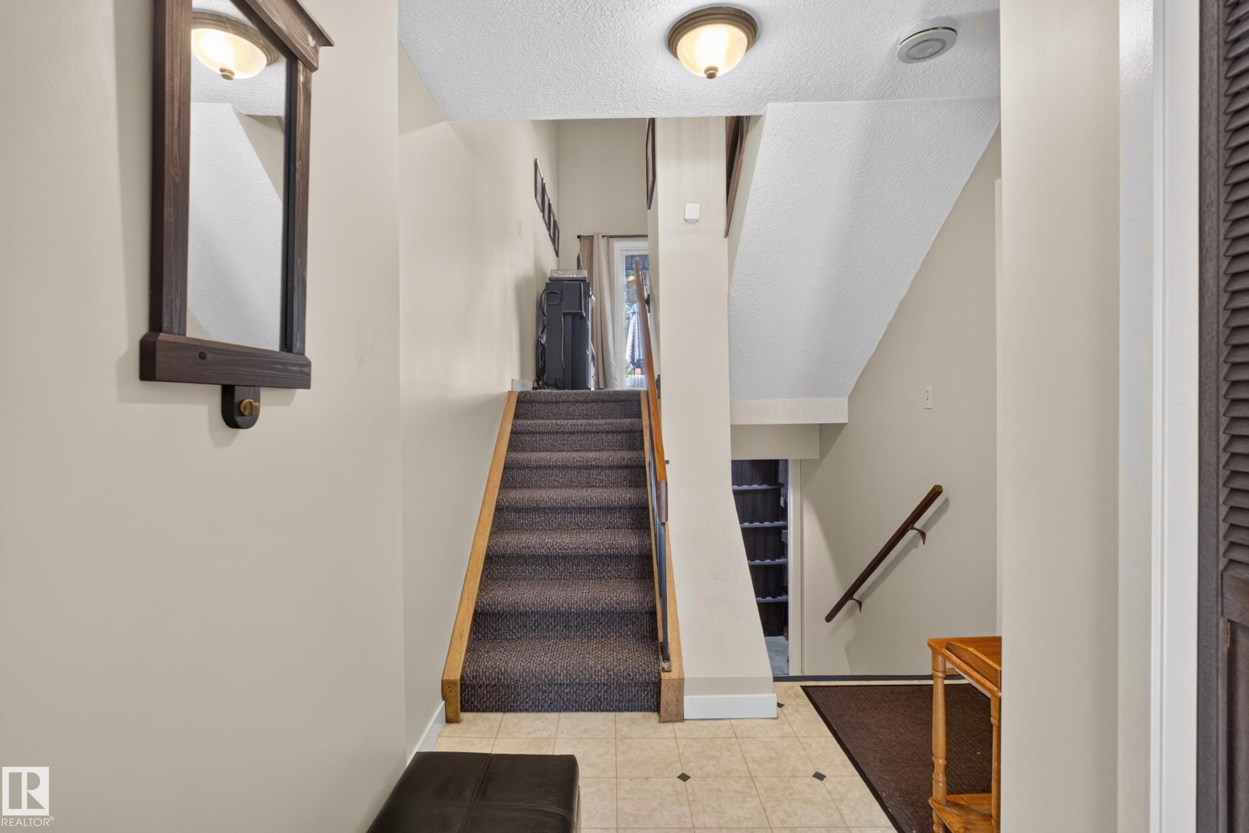 Entryway featuring tile flooring, a carpeted staircase with wood handrails, and a ceiling-mounted light fixture - 12062 157 Avenue, Edmonton, AB