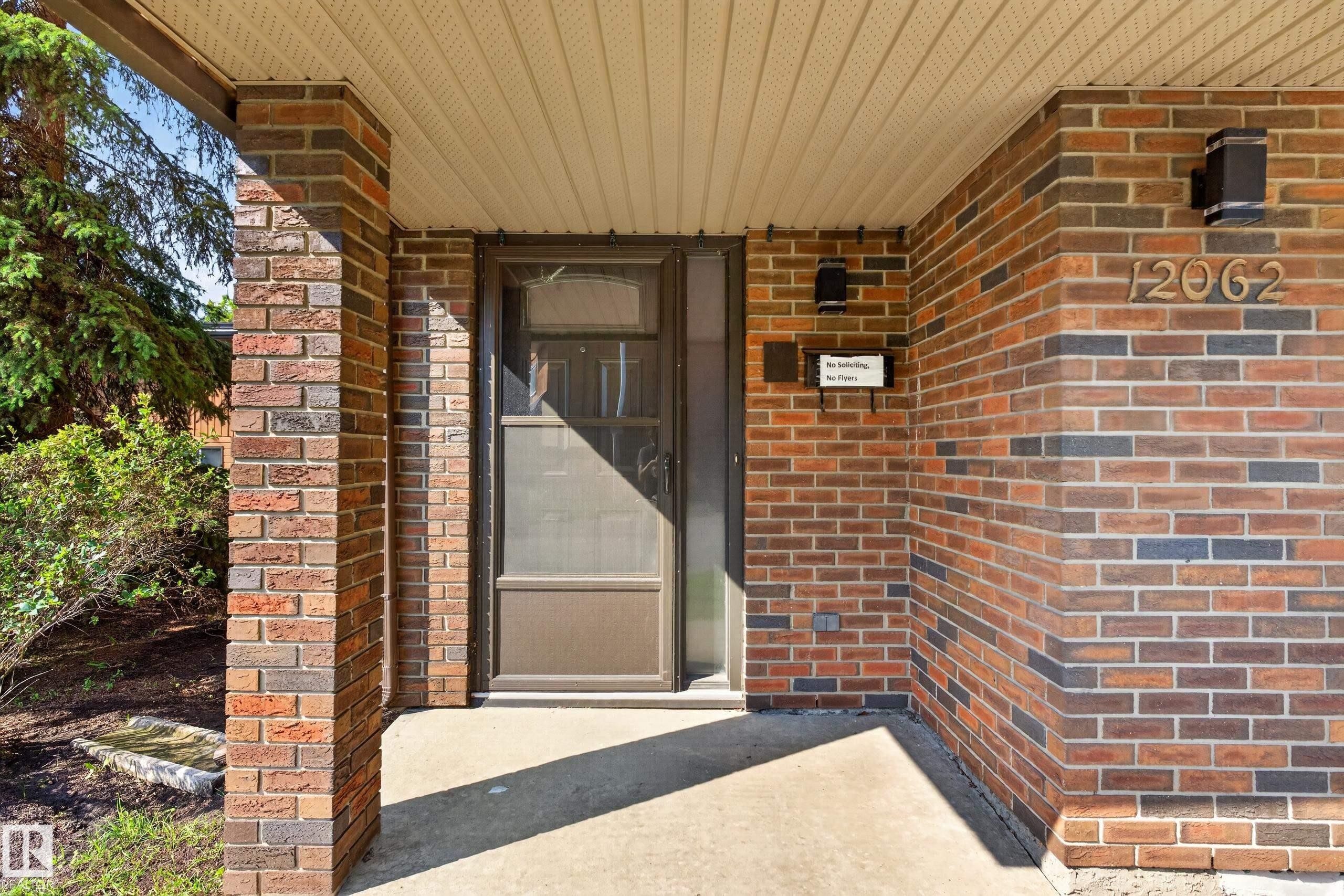 Brick exterior with an inviting front entry, covered porch, concrete flooring, and an entry door with a screen - 12062 157 Avenue, Edmonton, AB